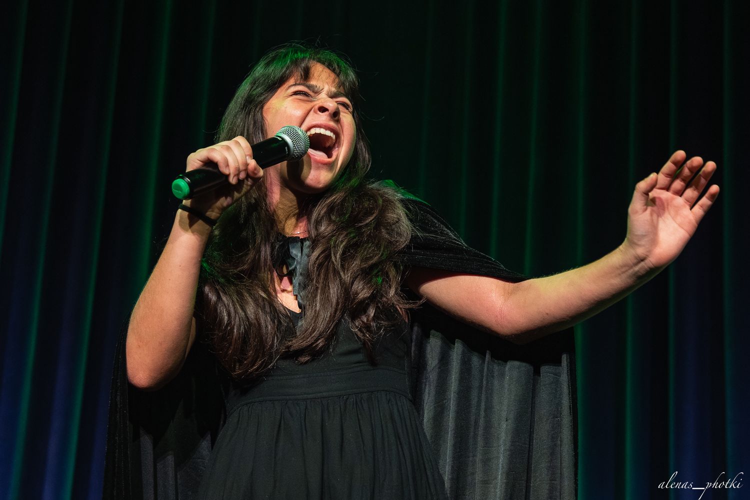 Performer sings passionately on stage with dramatic expressions against dark backdrop during live performance.