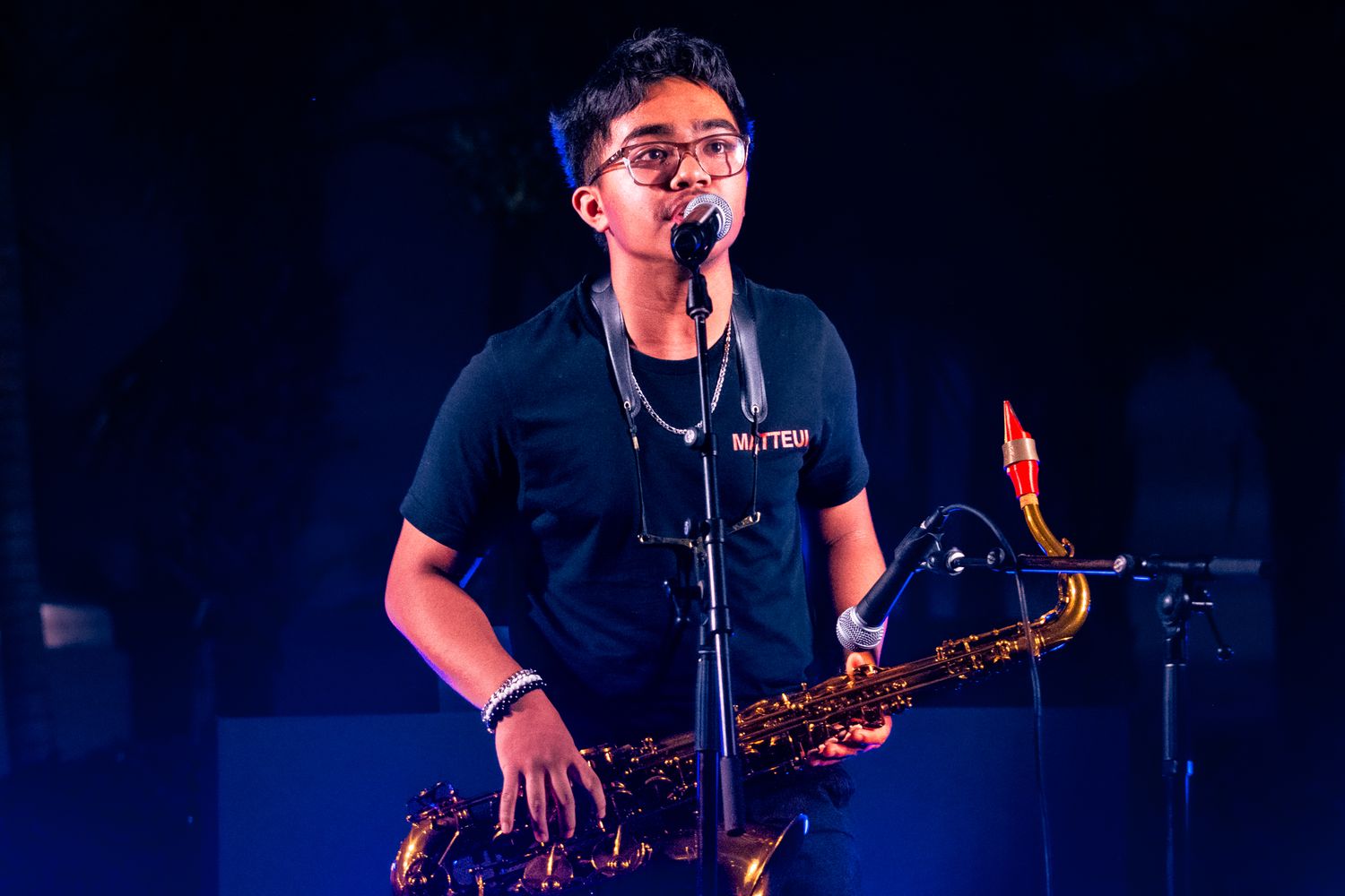 Saxophone player performs on stage with dark lighting and dramatic blue backlighting.