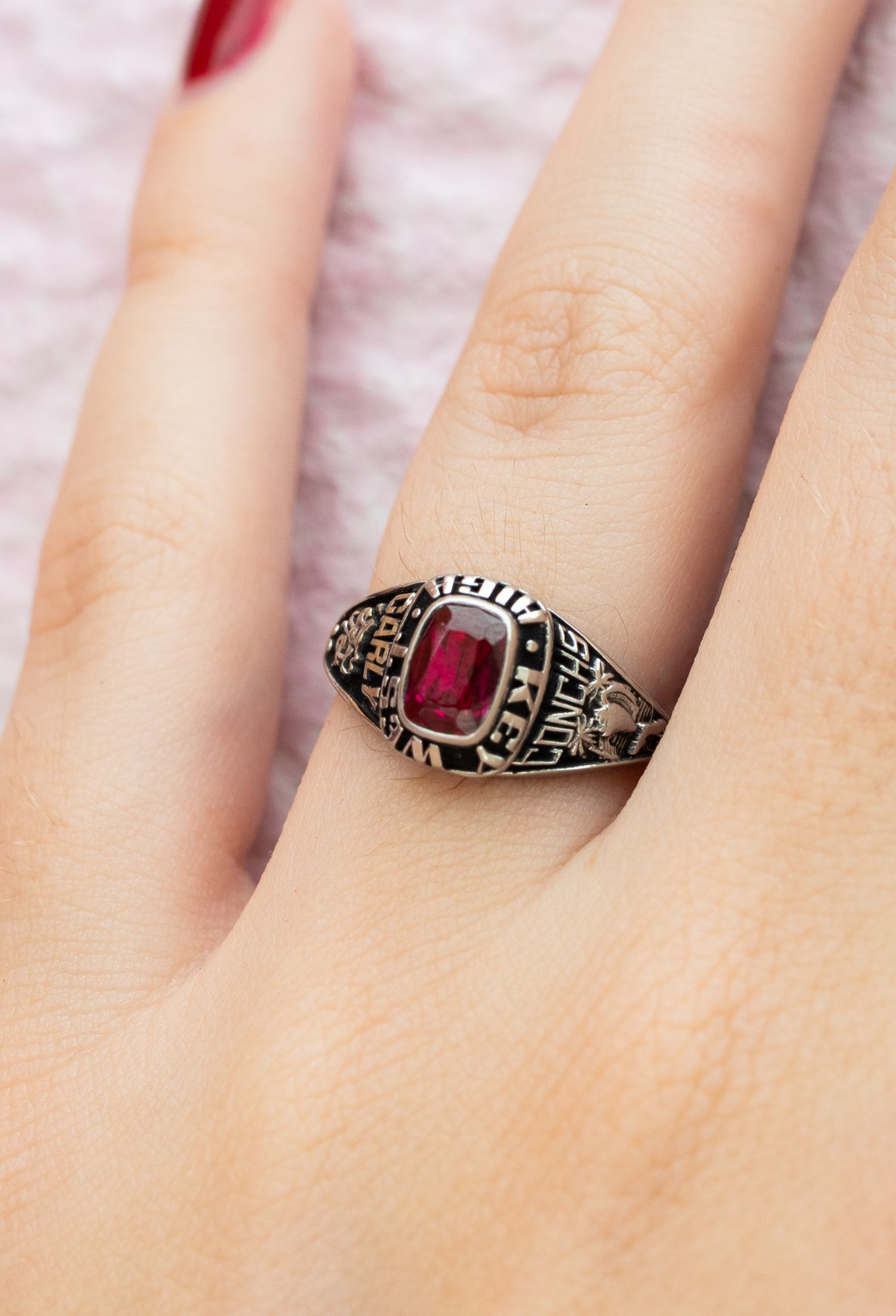 Close up view of a vintage-style ruby ring with ornate metalwork details on a person's hand.