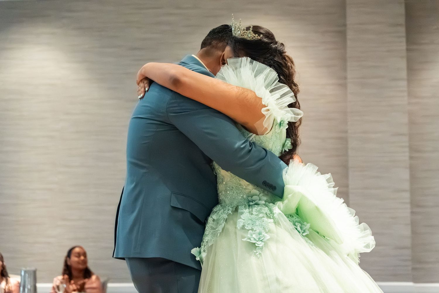 A couple shares a heartfelt embrace during a quinceañera dance, the girl wearing a elegant mint green ball gown.