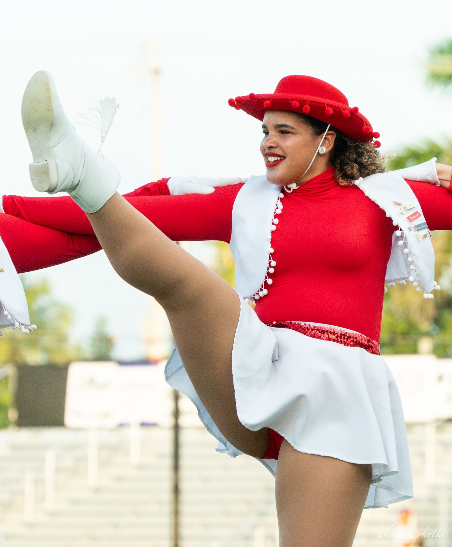 A cheerleader in red and white uniform performs a high kick at an outdoor event.