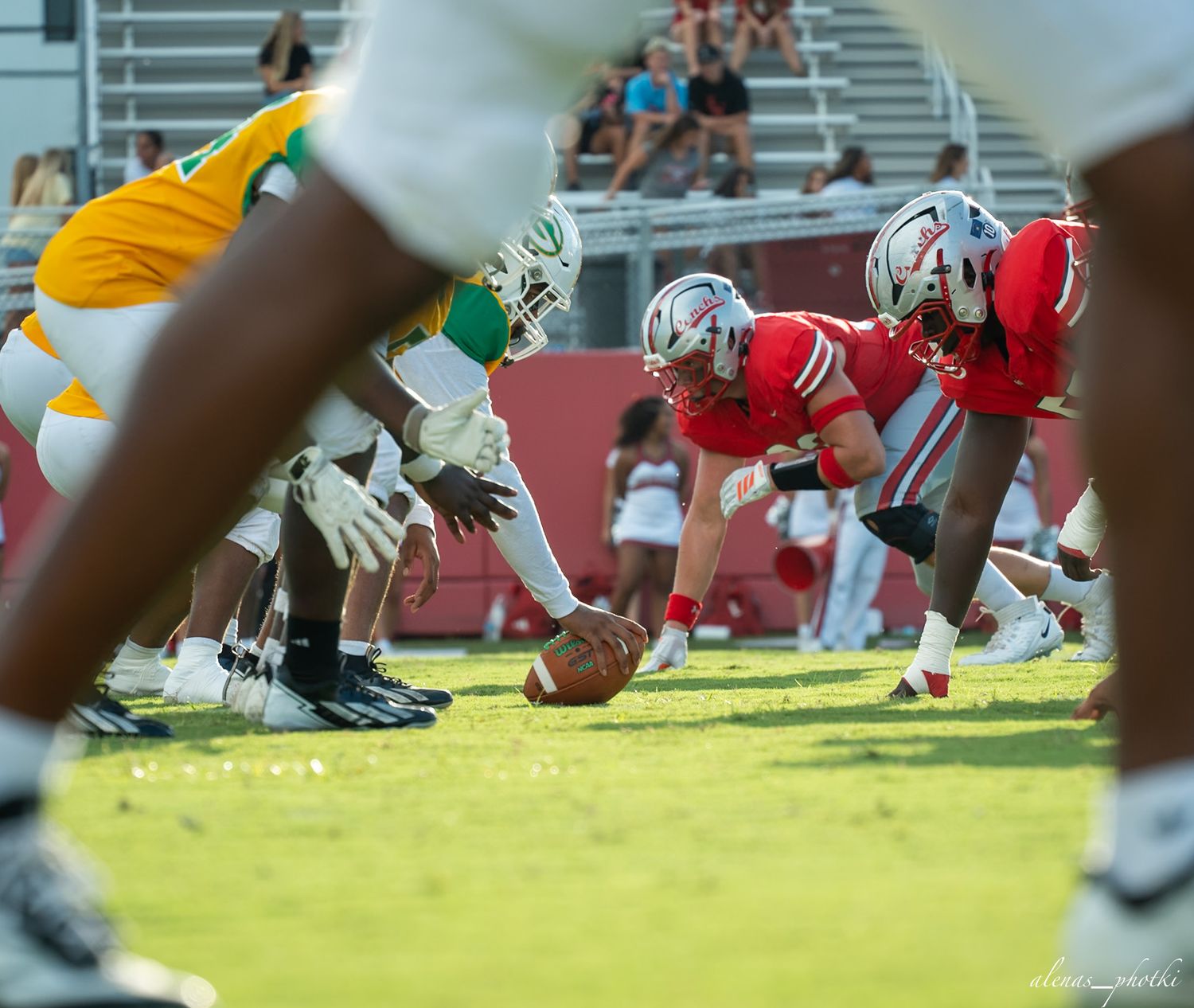 Red and green football teams face off at the line of scrimmage during a sunny outdoor game.