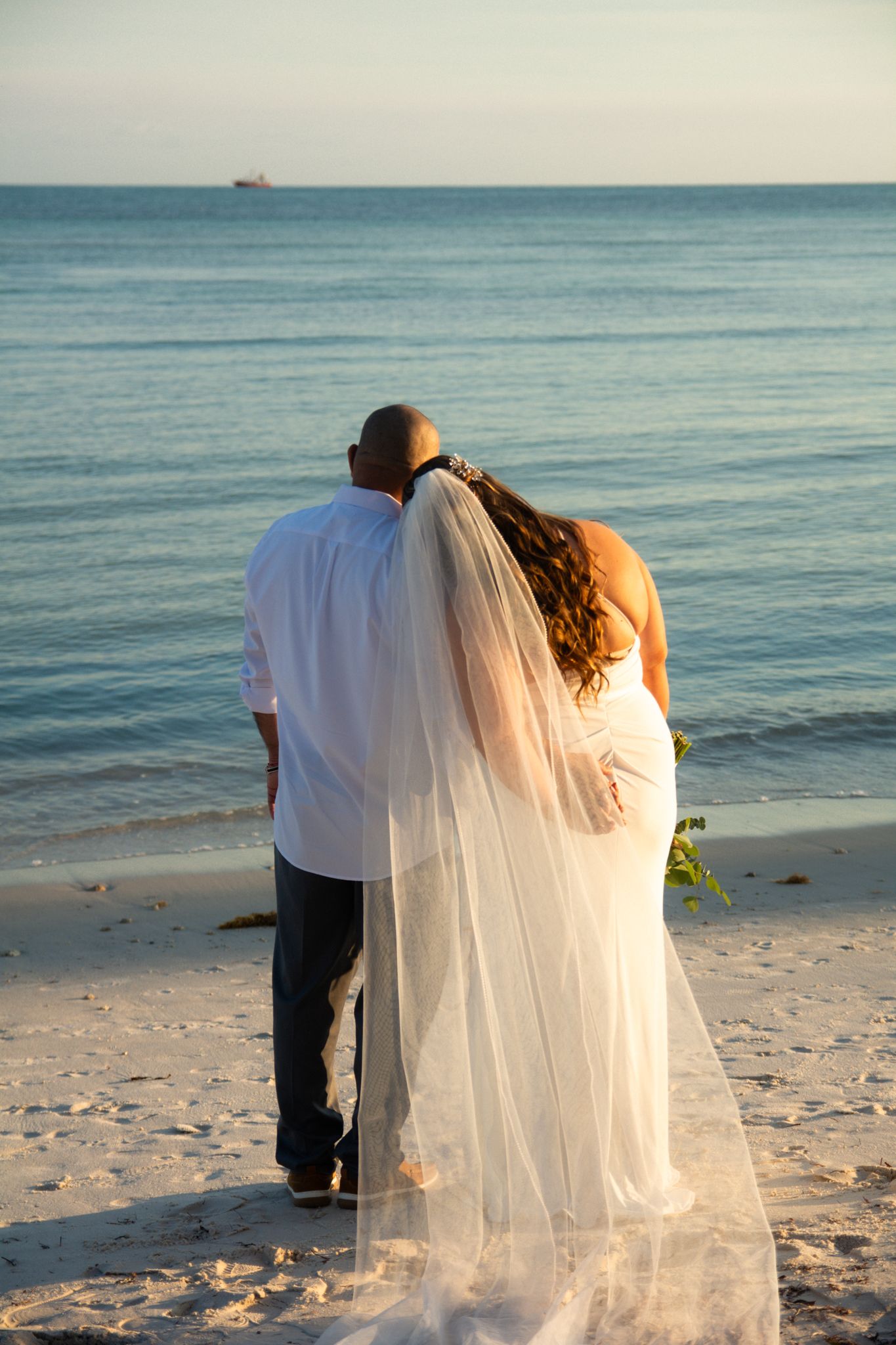 A couple gazes at the ocean during sunset on their beach wedding day.