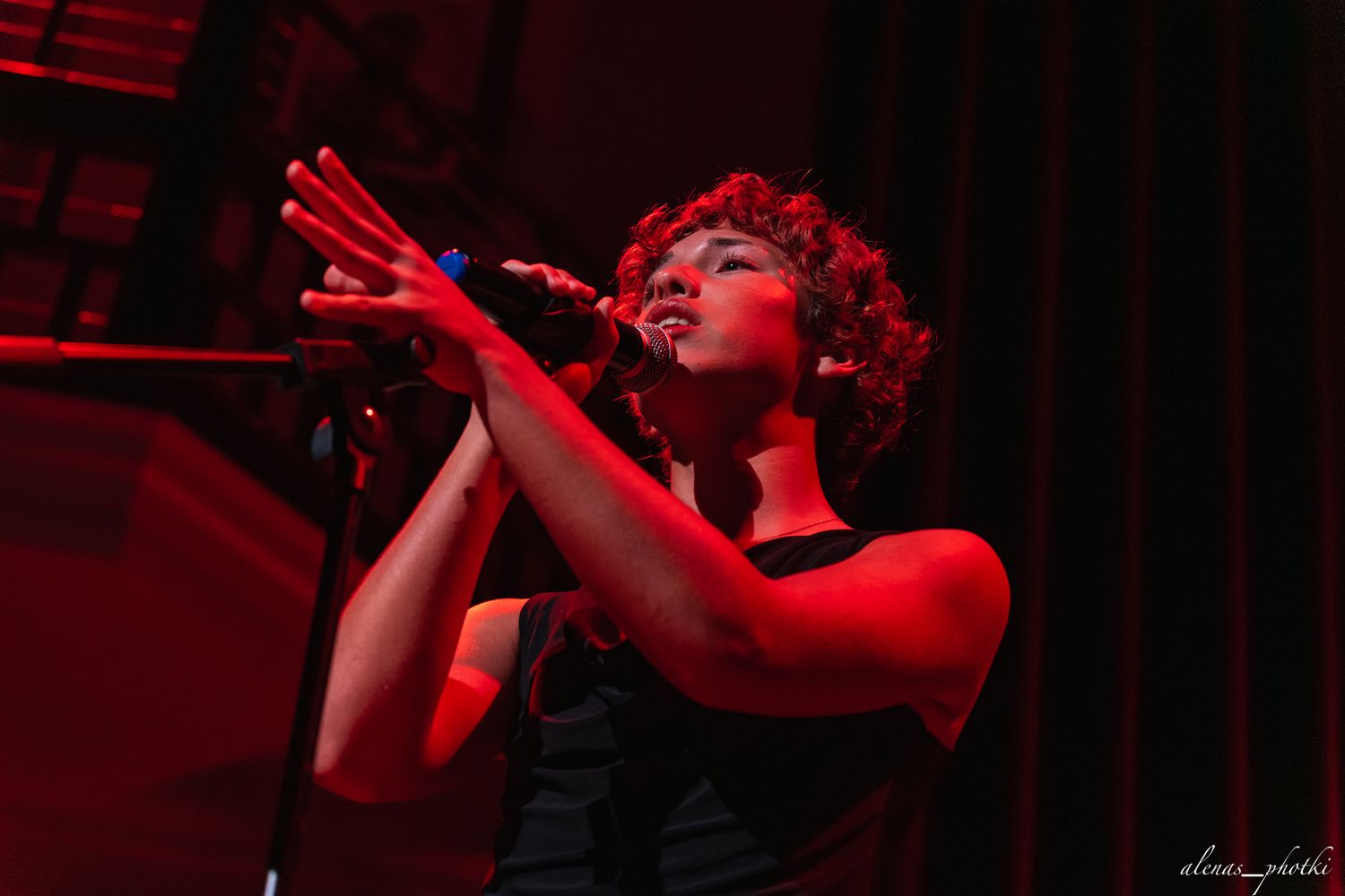 Performer in red lighting gestures dramatically on stage during an emotional musical performance.