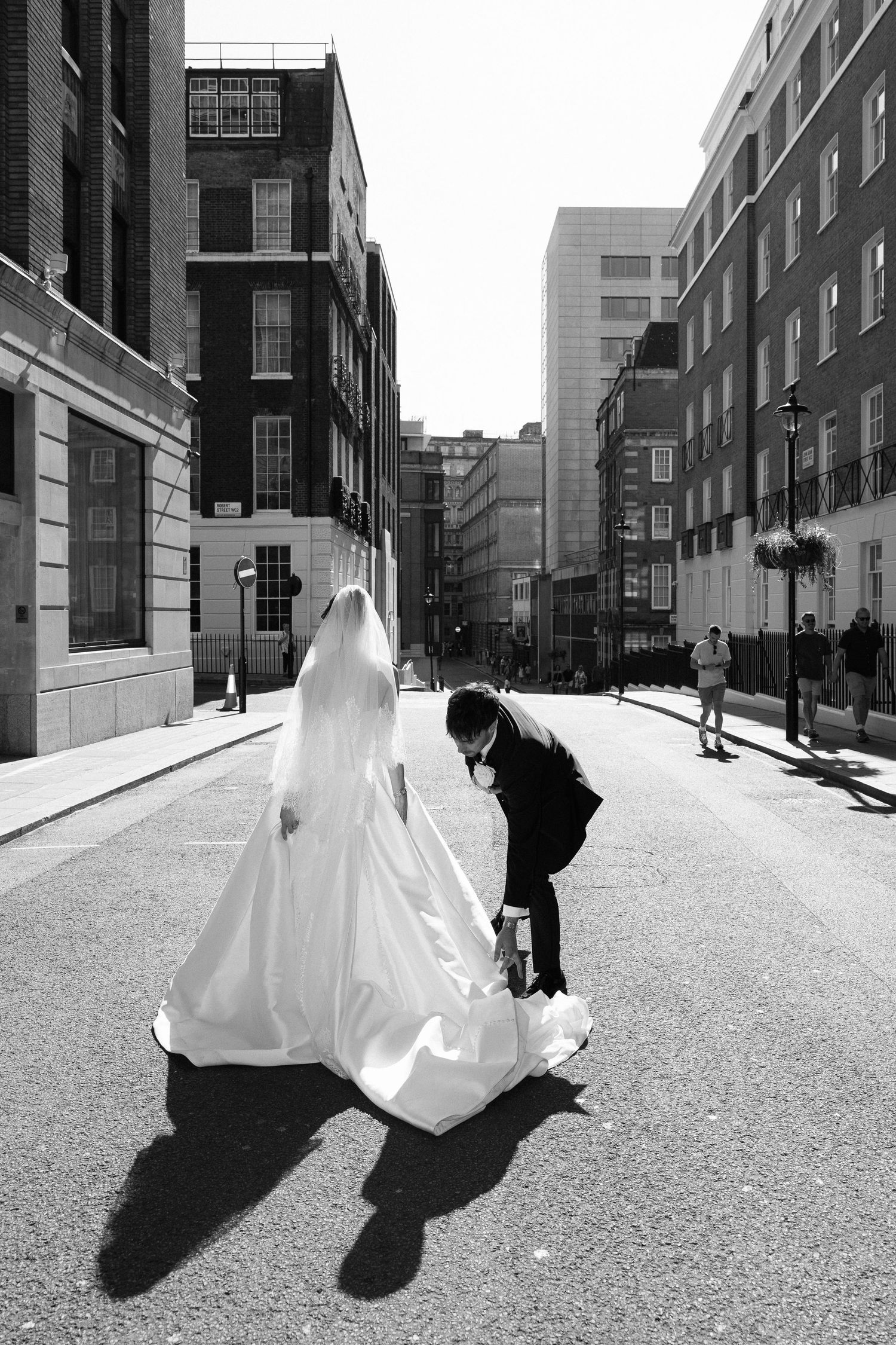 Black and white triptych shows a figure in flowing white fabric creating dramatic movement and shadows on an urban street.