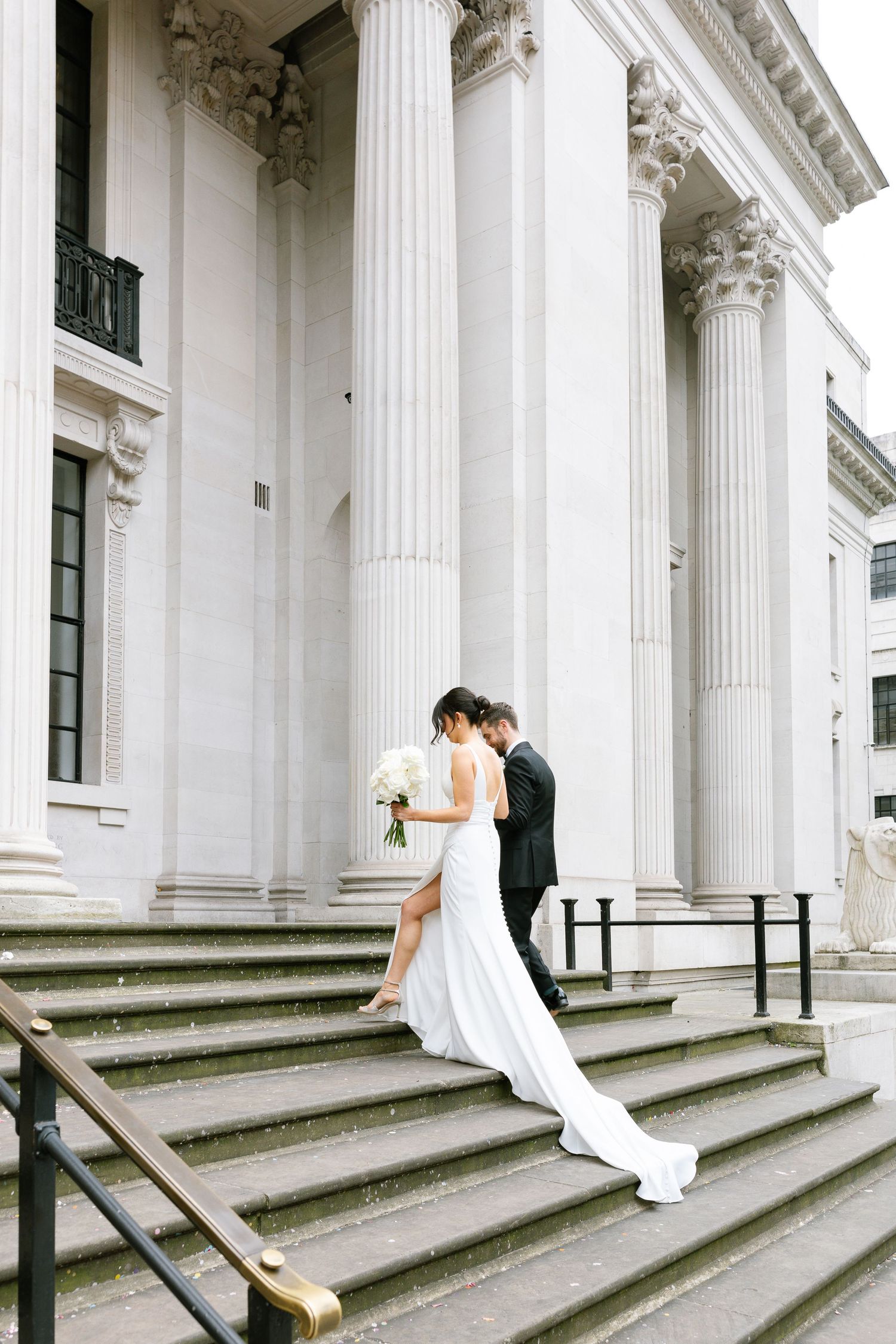 Romantic moment between newlyweds on classical building steps with white columns.