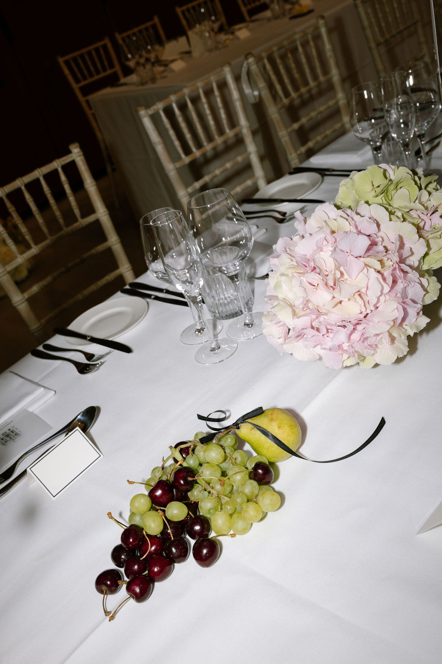 Formal table settings with white linens, crystal glasses, and elegant fruit and floral centerpieces in a banquet setting.