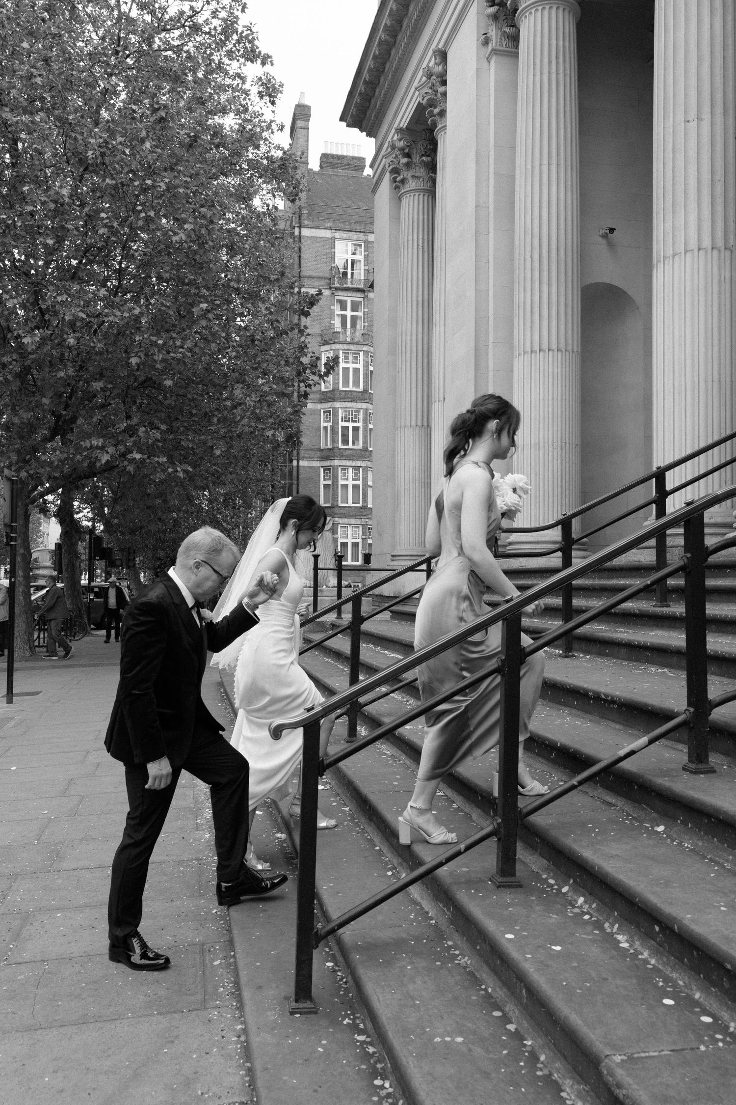 Wedding party ascending stone steps outside a classic columned building, MARYLEBONE Town Hall