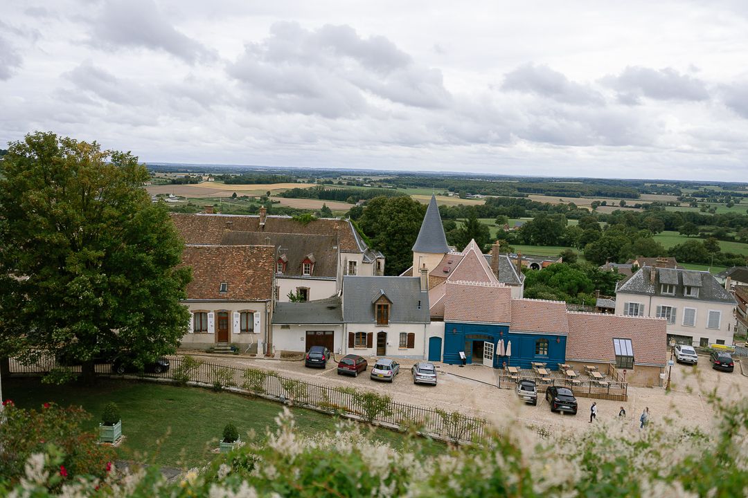 Panoramic aerial view of small town buildings and streets surrounded by green rural landscape under cloudy skies.