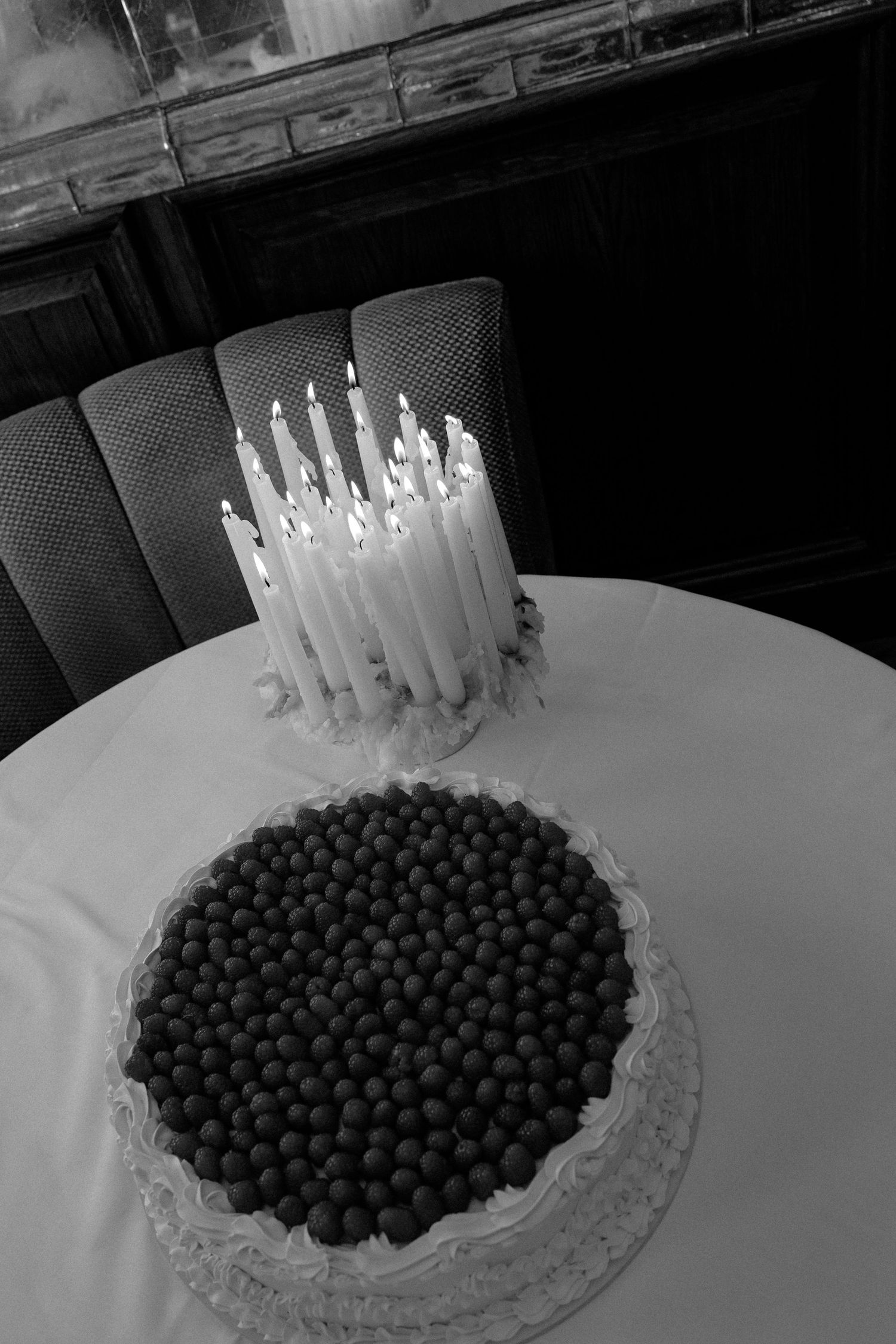 Black and white photo of birthday cake topped with lit candles and chocolate pearls.