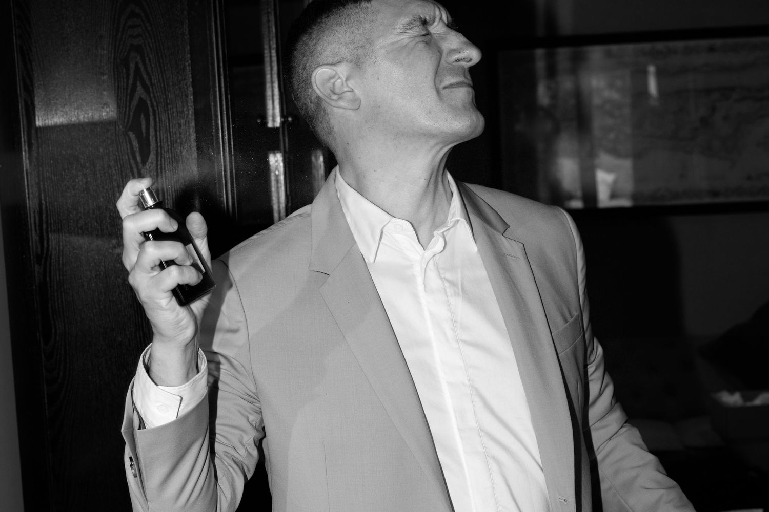A person in a white dress shirt laughs joyfully while holding a microphone in a dimly lit setting.