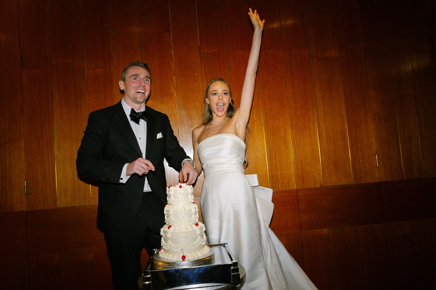 A happy couple celebrates during their wedding reception in a warm-lit wooden paneled venue.