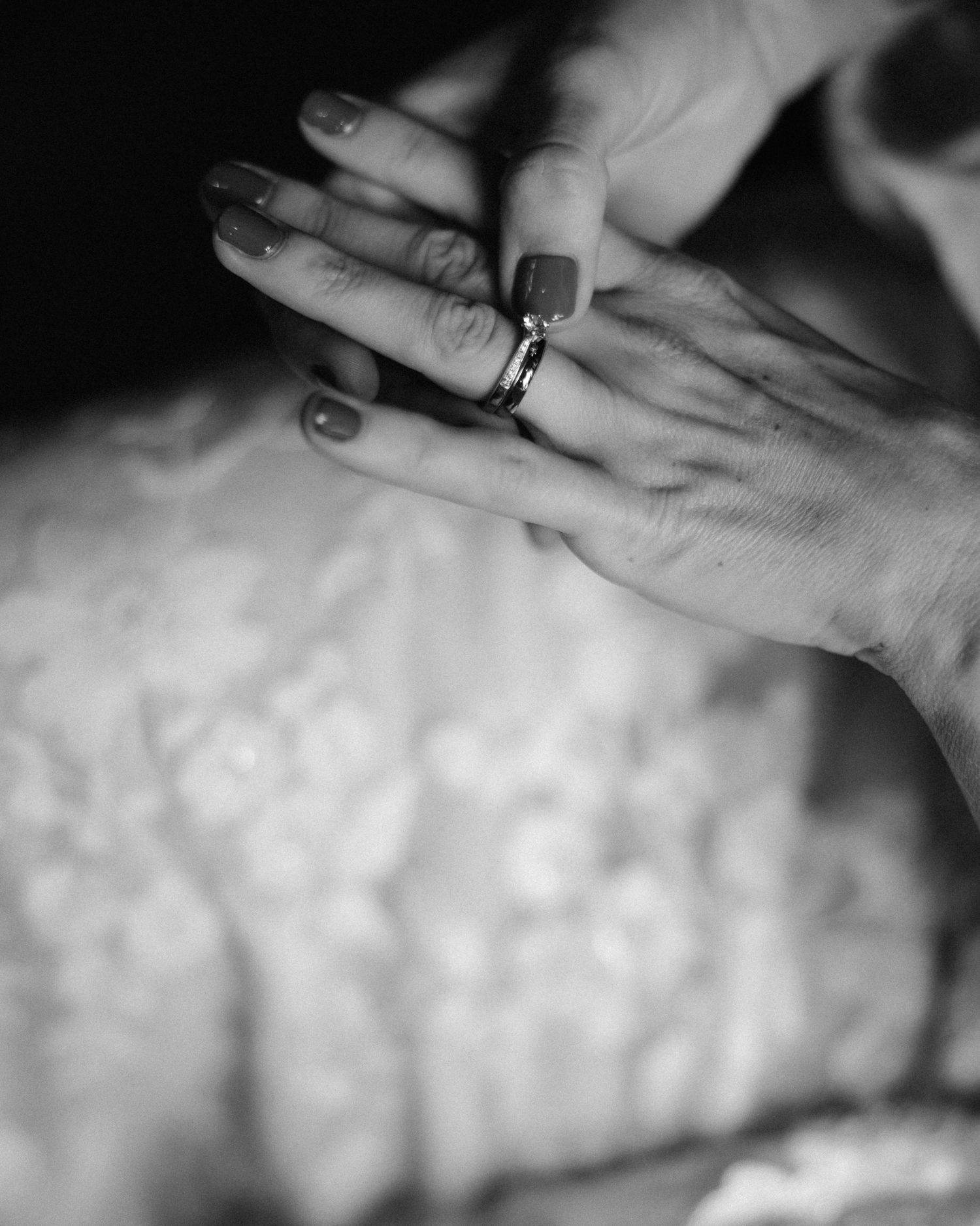 Close-up black and white photo of hands showing engagement or wedding rings.