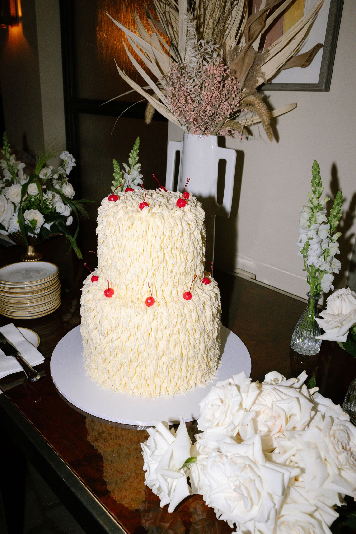 Two-tiered white wedding cake decorated with textured frosting and dried floral topper.