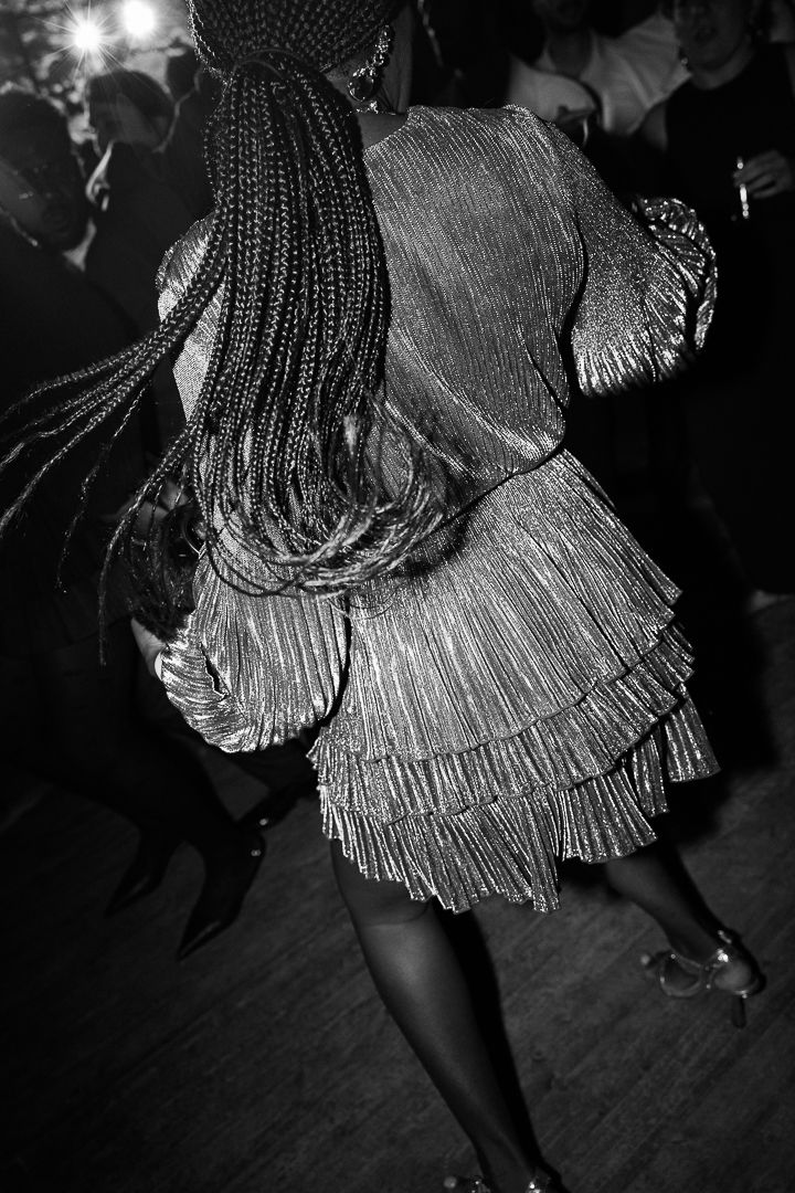 A black and white photograph shows a dancer in a fringed dress twirling on a dance floor.