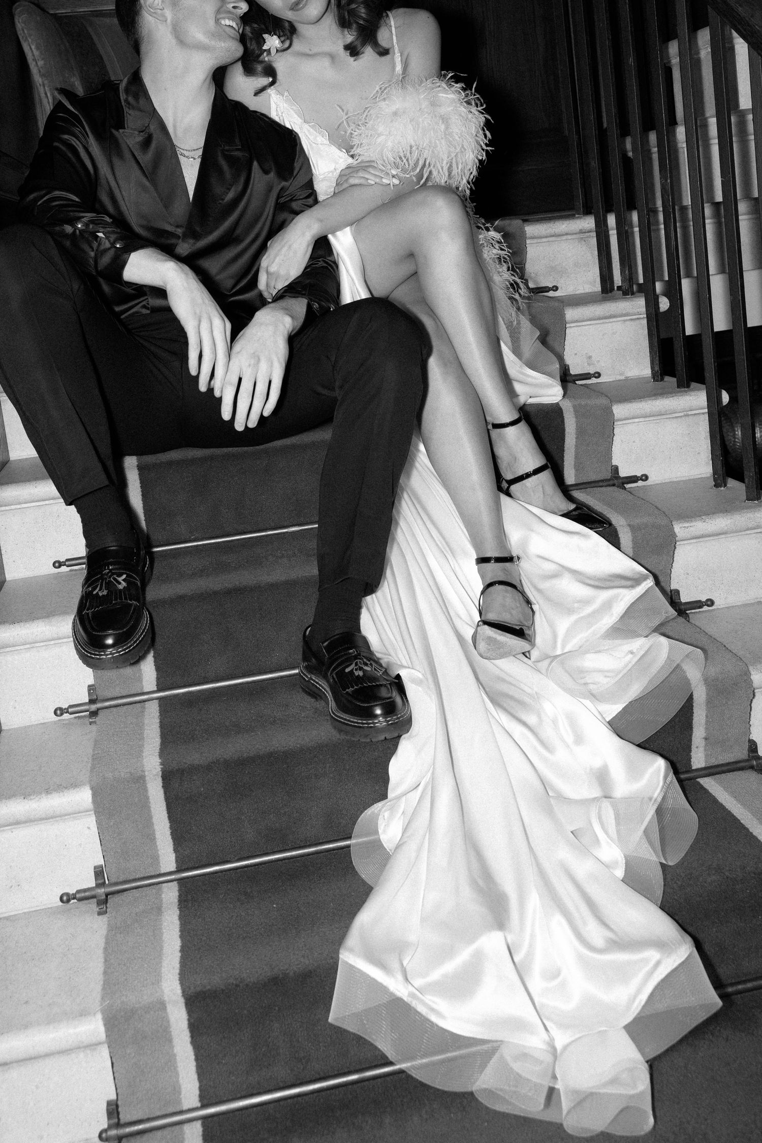 A dramatic black and white shot of a bride and groom sitting on elegant carpeted stairs.