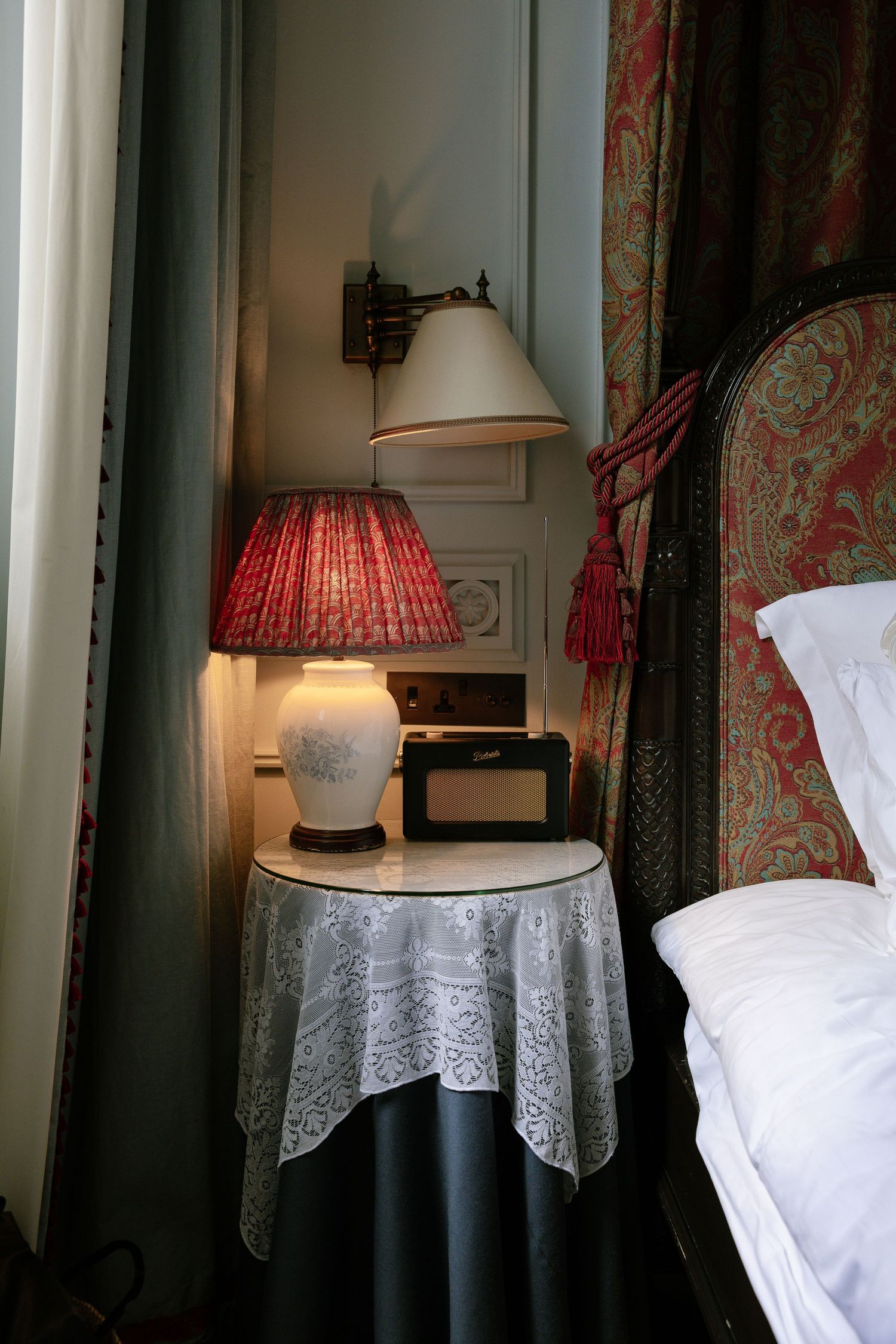 Vintage bedroom interior with lace tablecloths, table lamps, and floral wallpaper creating a cozy nostalgic atmosphere.