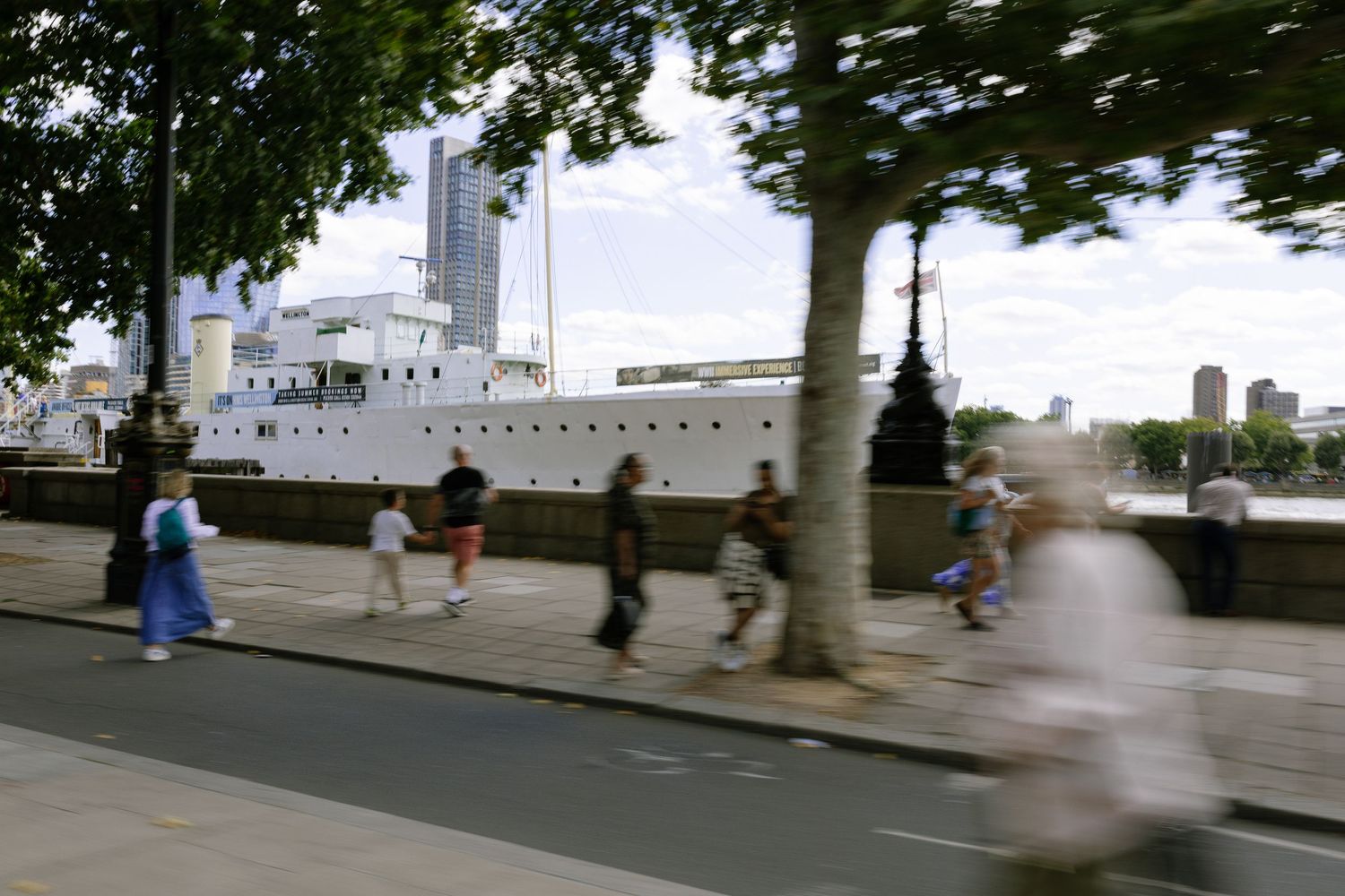 A person walks along London's South Bank riverside path with trees and buildings visible in the background.