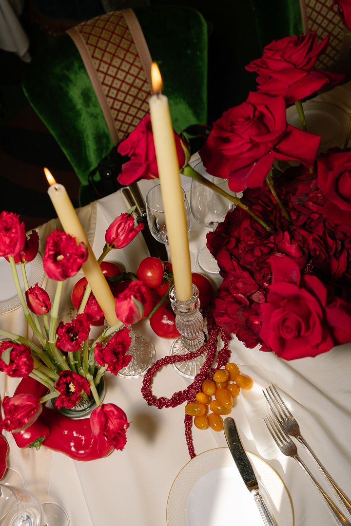 Elegant table setting with red roses, cream candles, and crystal glassware creates a romantic dining atmosphere.