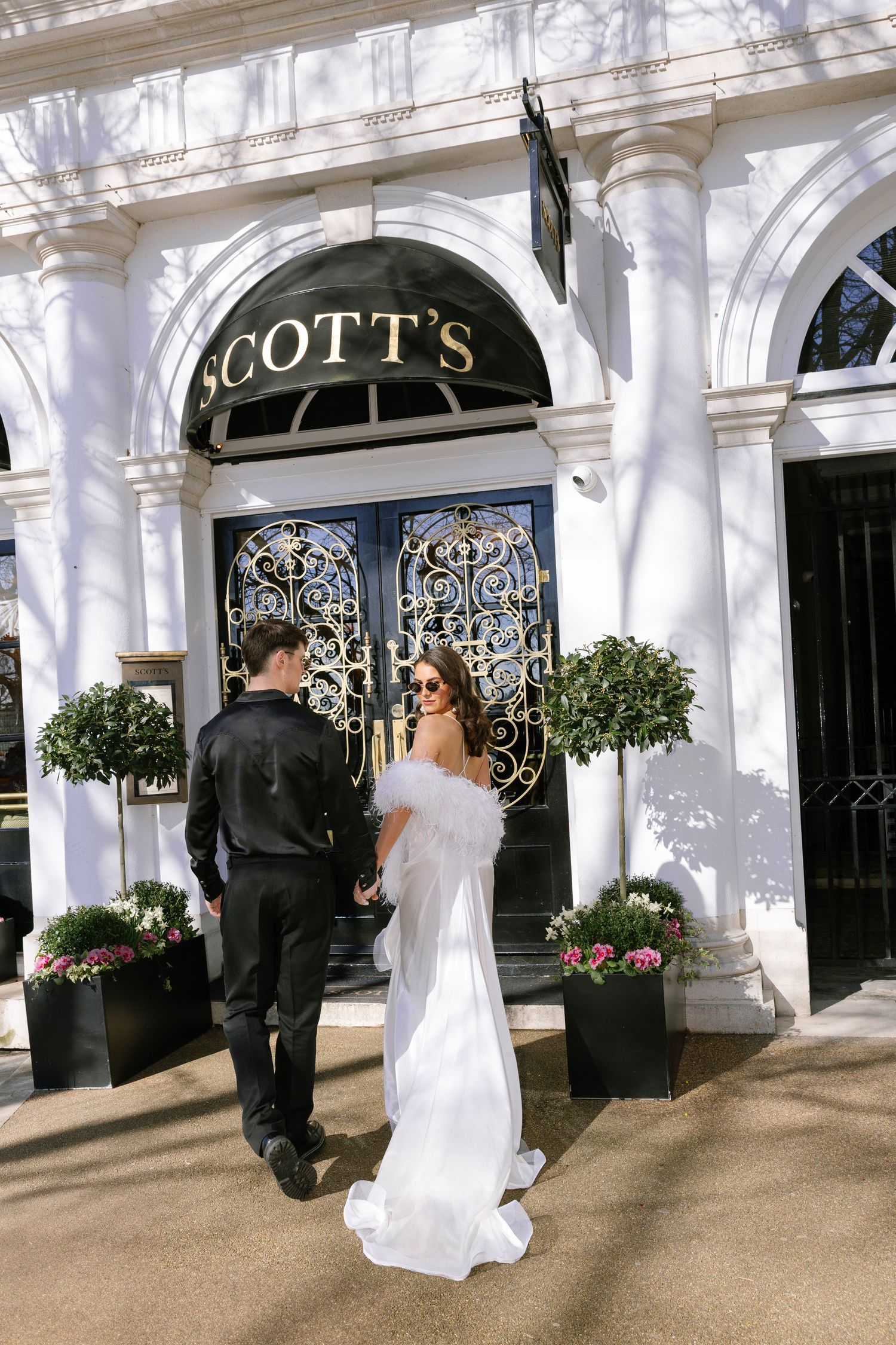 Couple entering Scott's venue with ornate iron gates and potted plants framing elegant entrance.