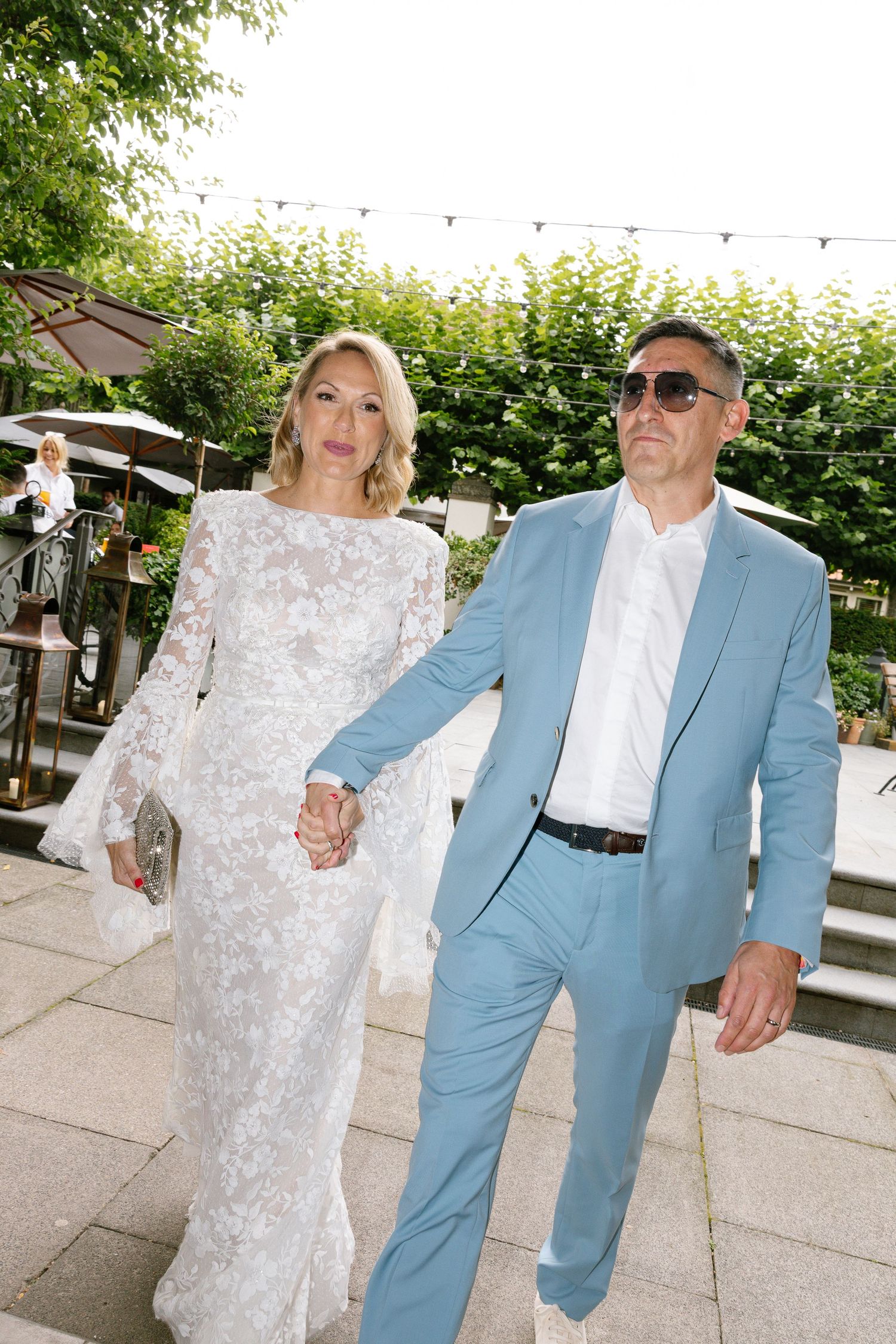 A couple in a light blue suit and white lace dress share candid moments together during an outdoor event.