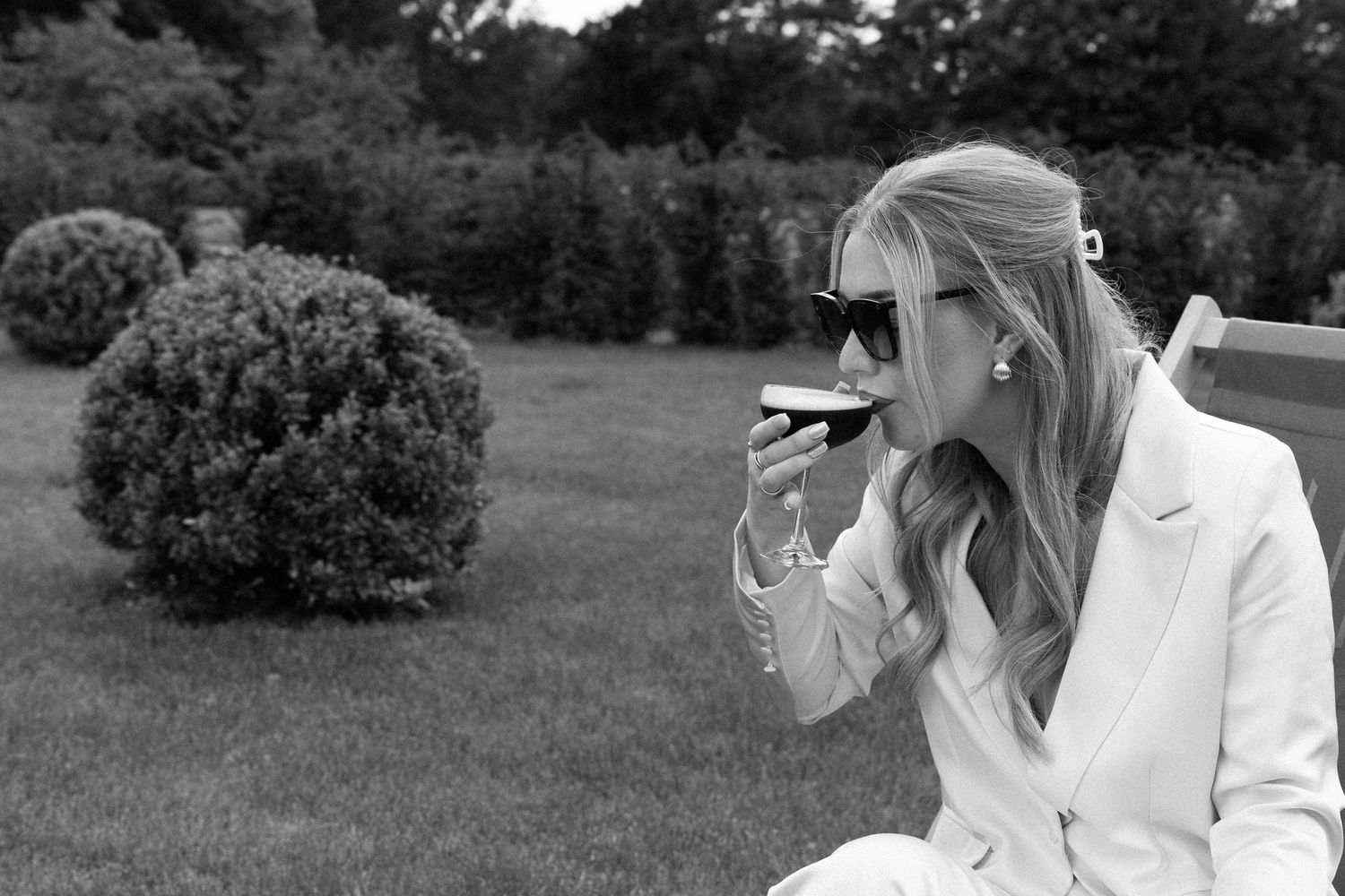 Woman in white blazer smoking a cigarette outdoors in black and white photography.