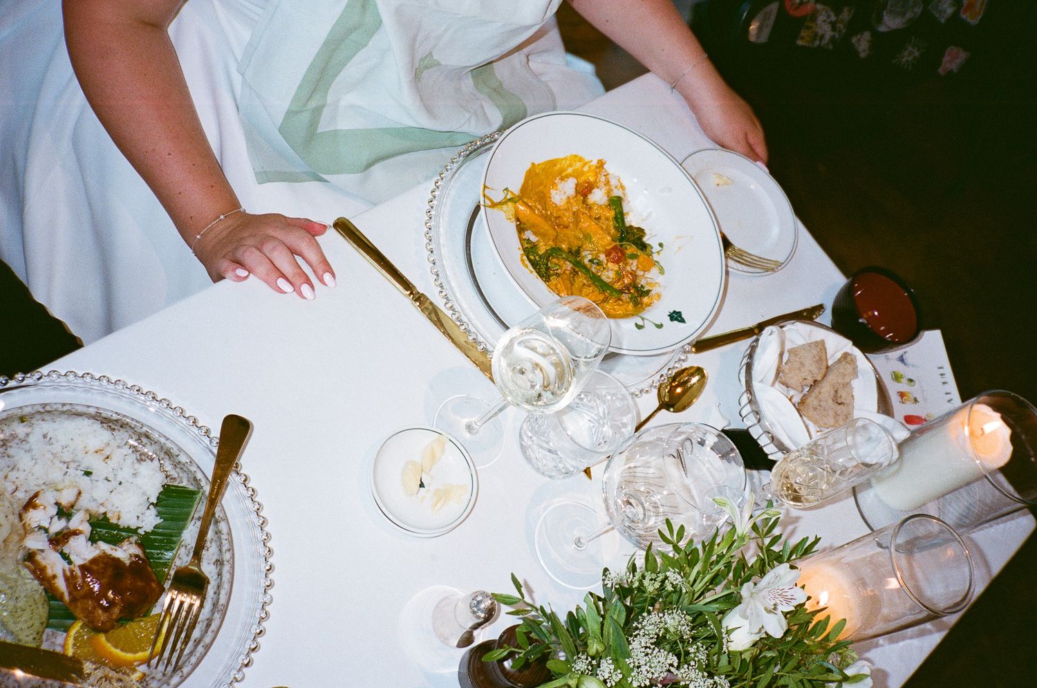 Overhead view of hands reaching for plates at a dinner table with white linens and colorful dishes.