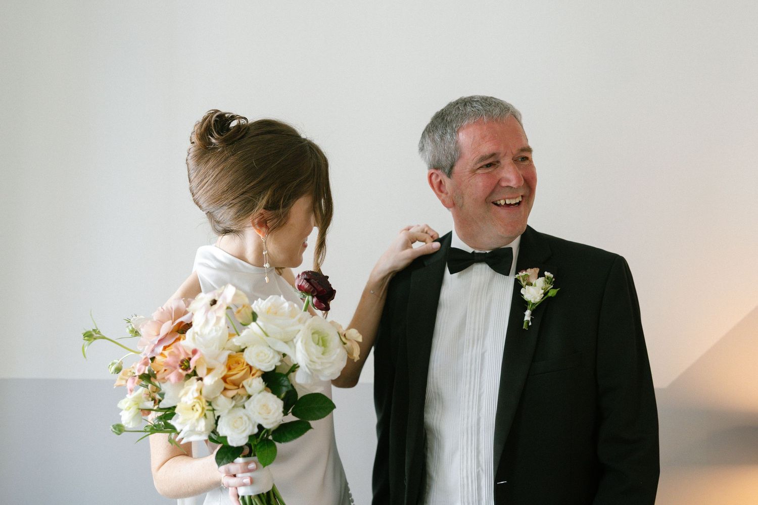 A sweet moment between family members at a wedding as the person in black tie wears a boutonniere and smiles.