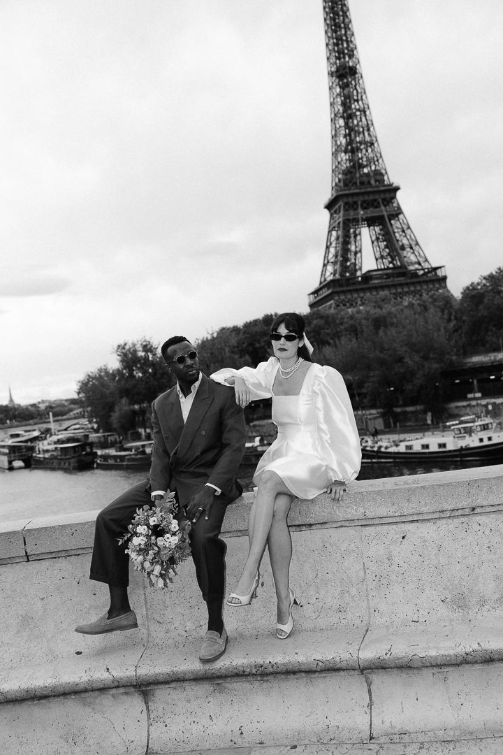A couple sits together on a wall near the Eiffel Tower in Paris in a series of black and white photographs.