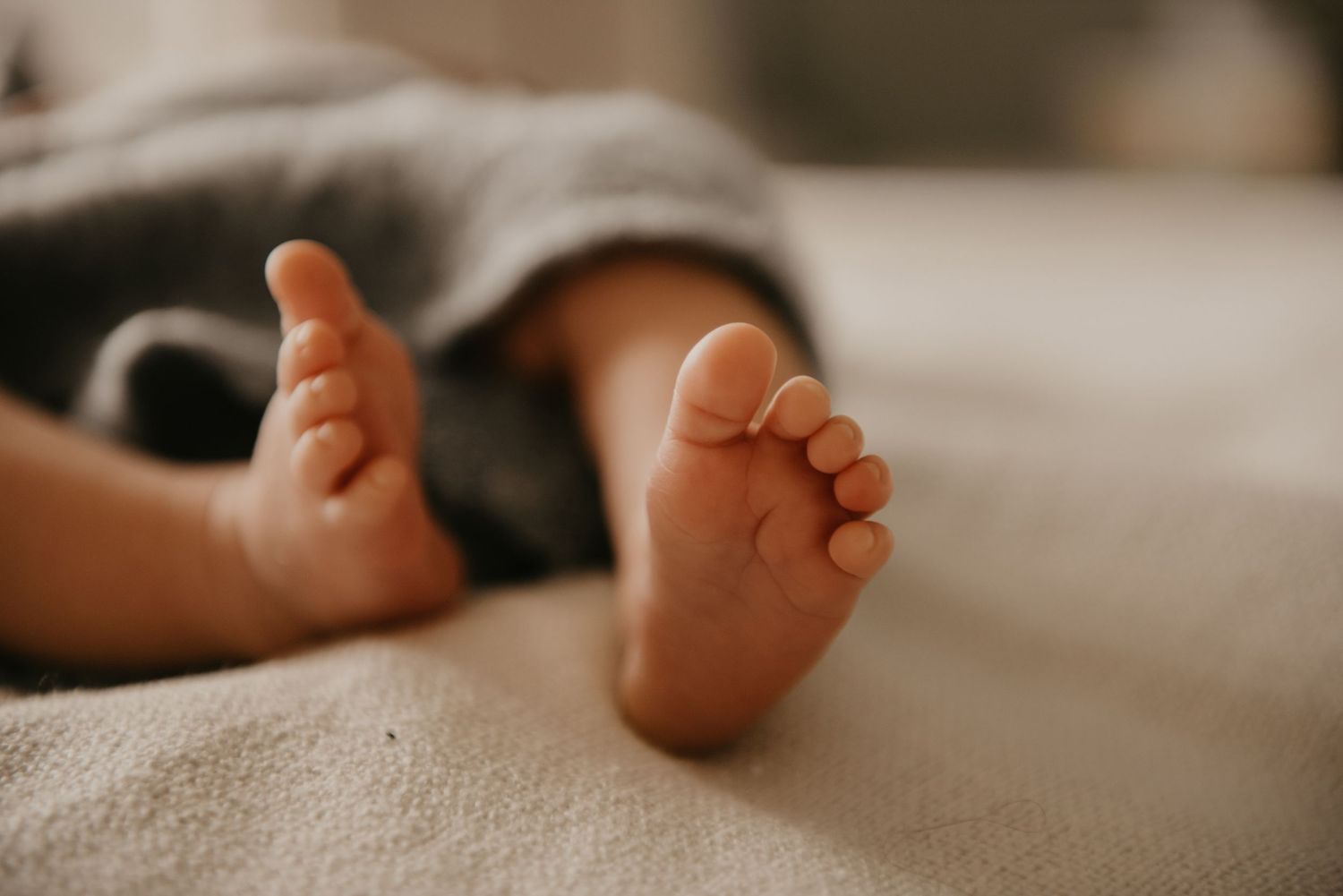 Close-up of tiny baby feet resting on soft white bedding.