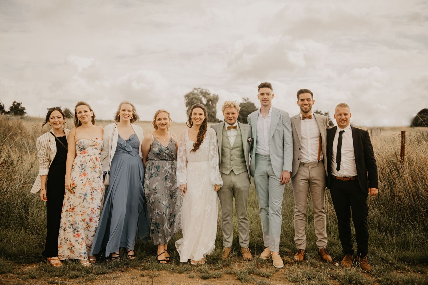 Wedding party poses together in a rustic outdoor setting with warm tones and natural lighting.