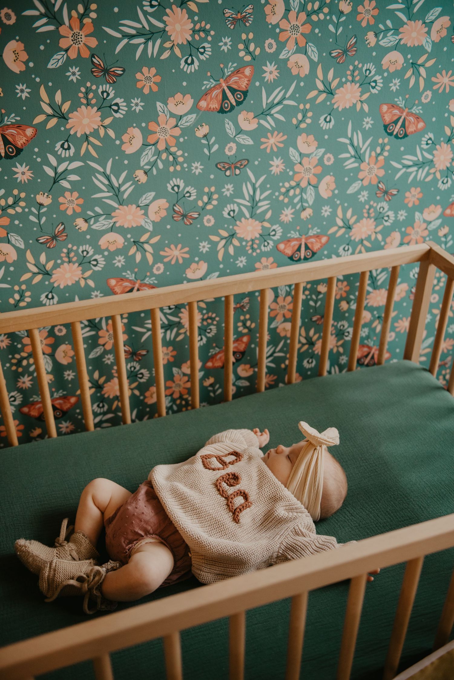 Baby sleeping peacefully in a crib with floral wallpaper backdrop.