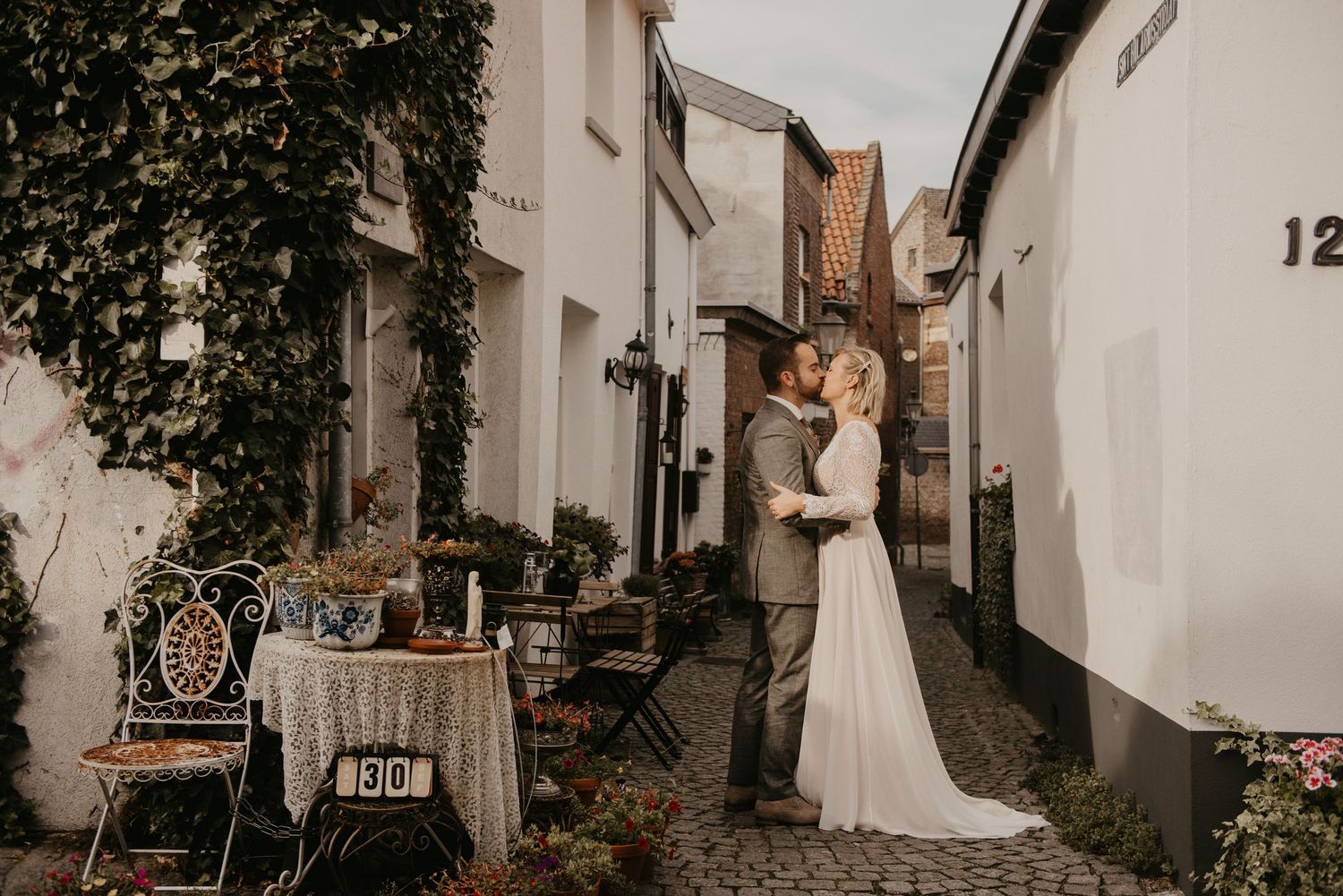 Newlyweds walking through a charming European alleyway with white buildings.