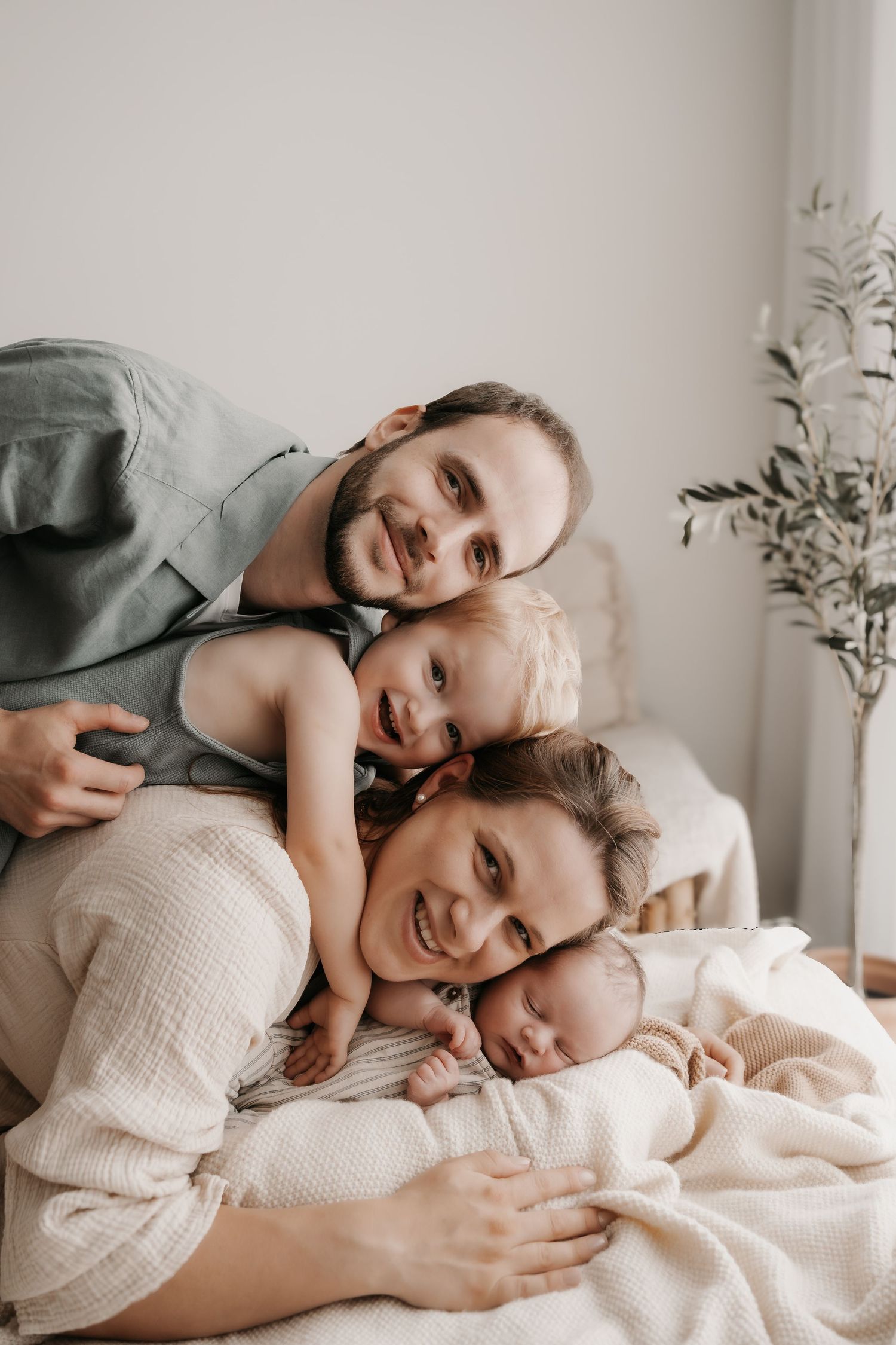 Family sharing a moment while lying on white bedding in natural light.