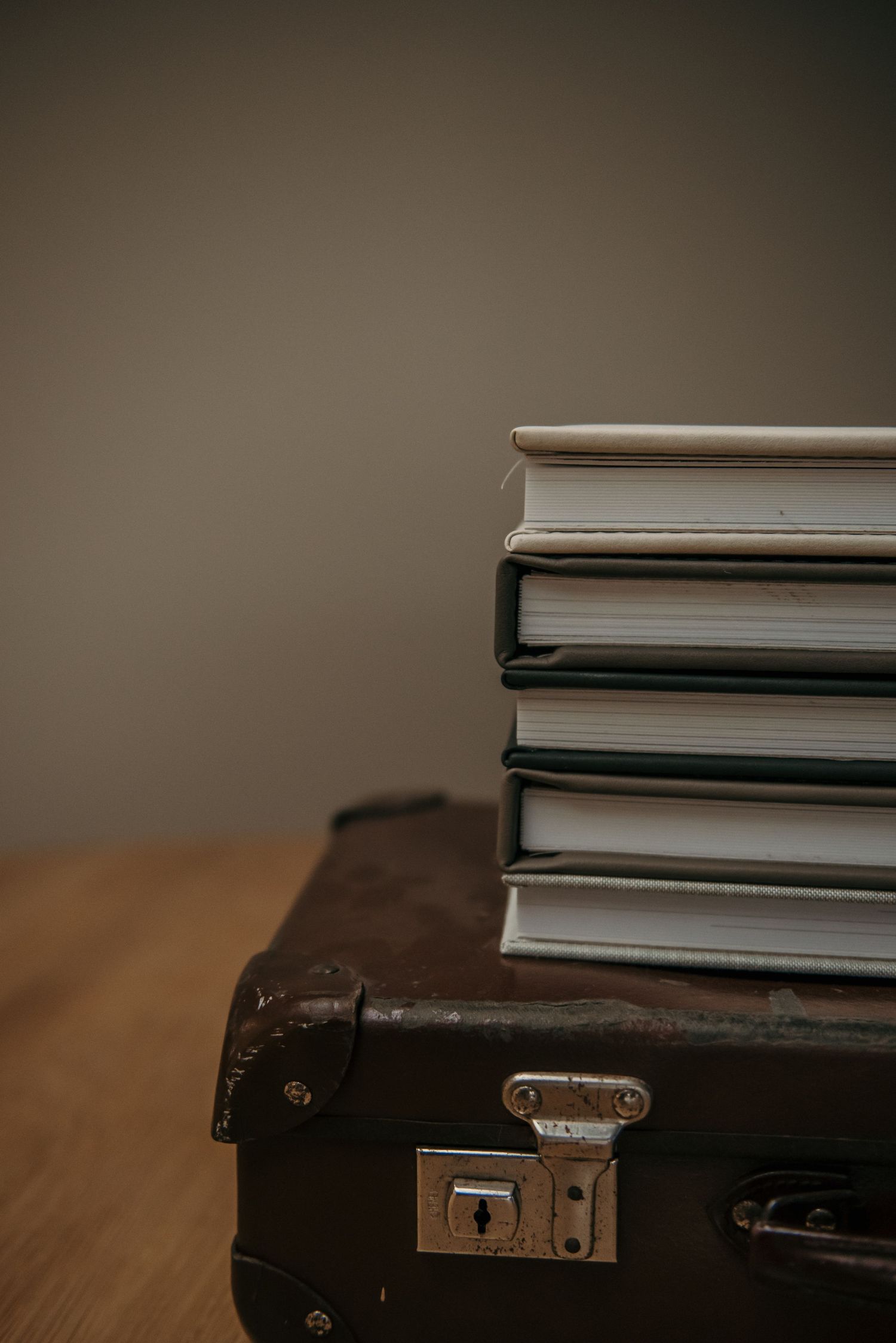 Stack of professional photo albums and vintage leather case on wooden surface.