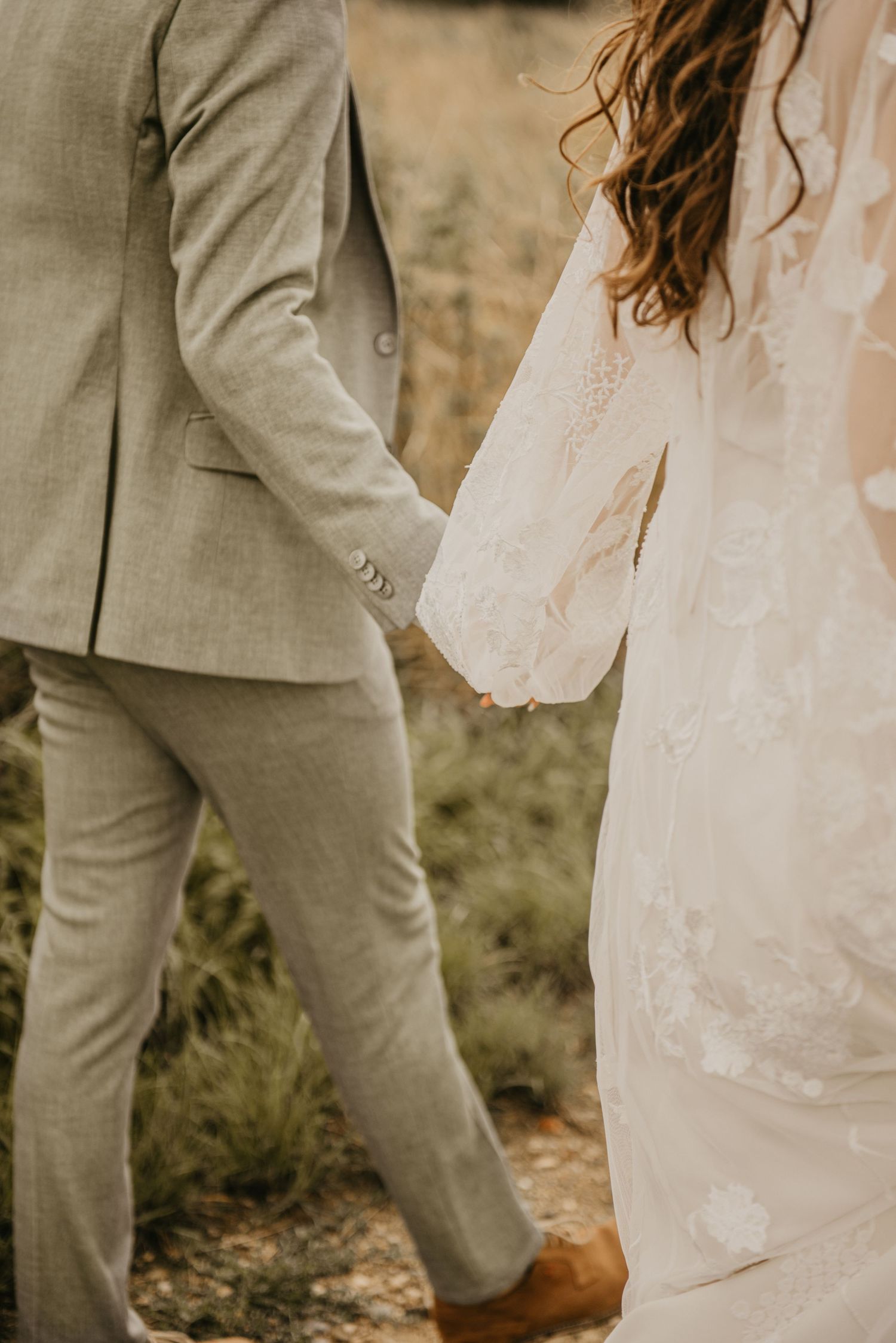 Detail shot of bride's white lace dress and groom's light suit during outdoor wedding.