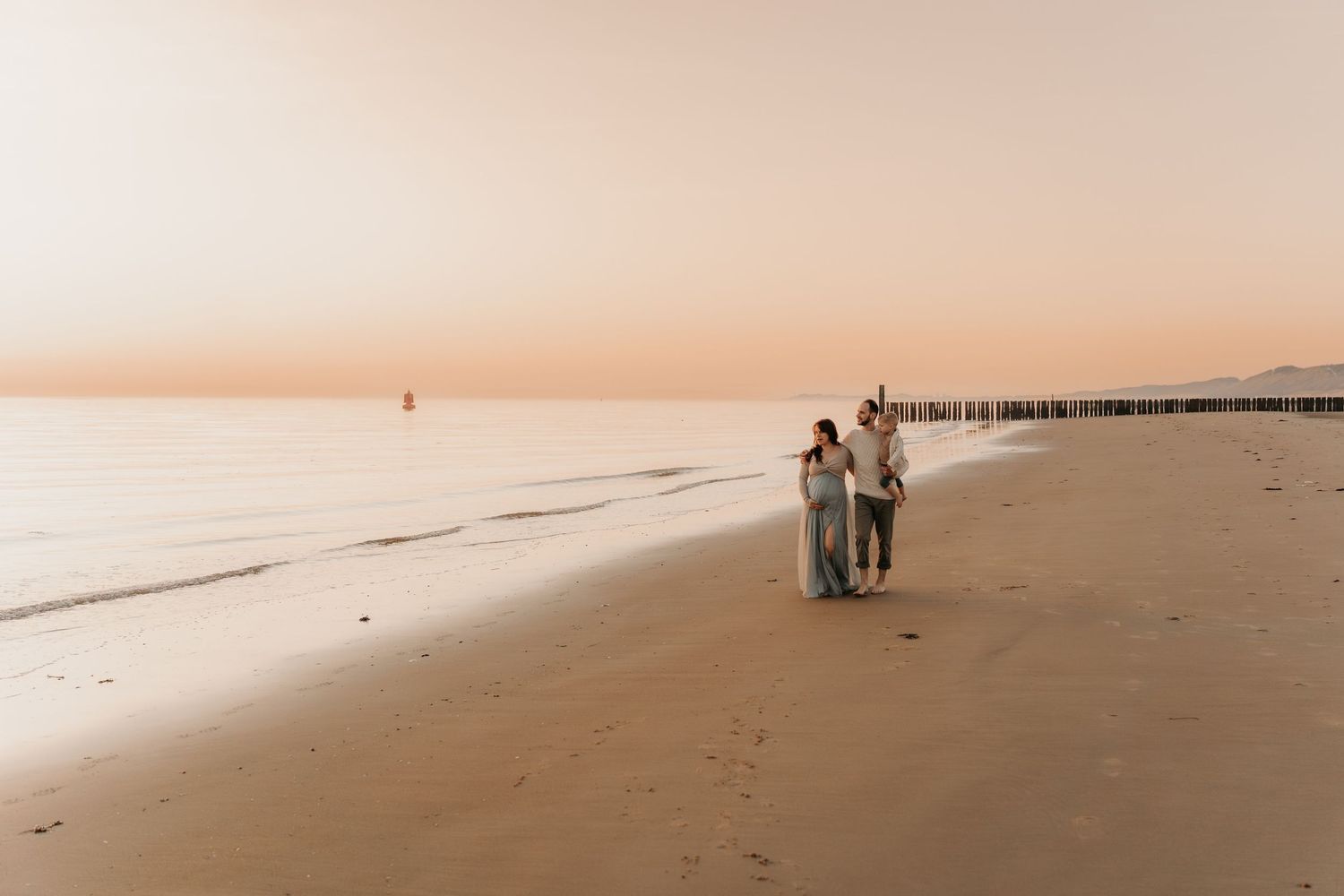Minimalist beach landscape with soft peachy tones and distant figures walking along shoreline.