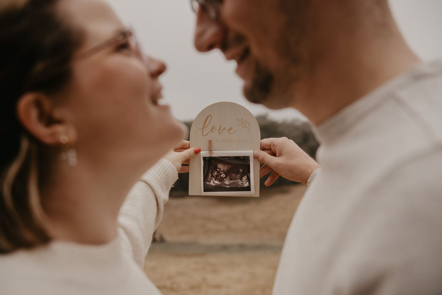 Couple in light colored clothing sharing tender moment while holding ultrasound photo.