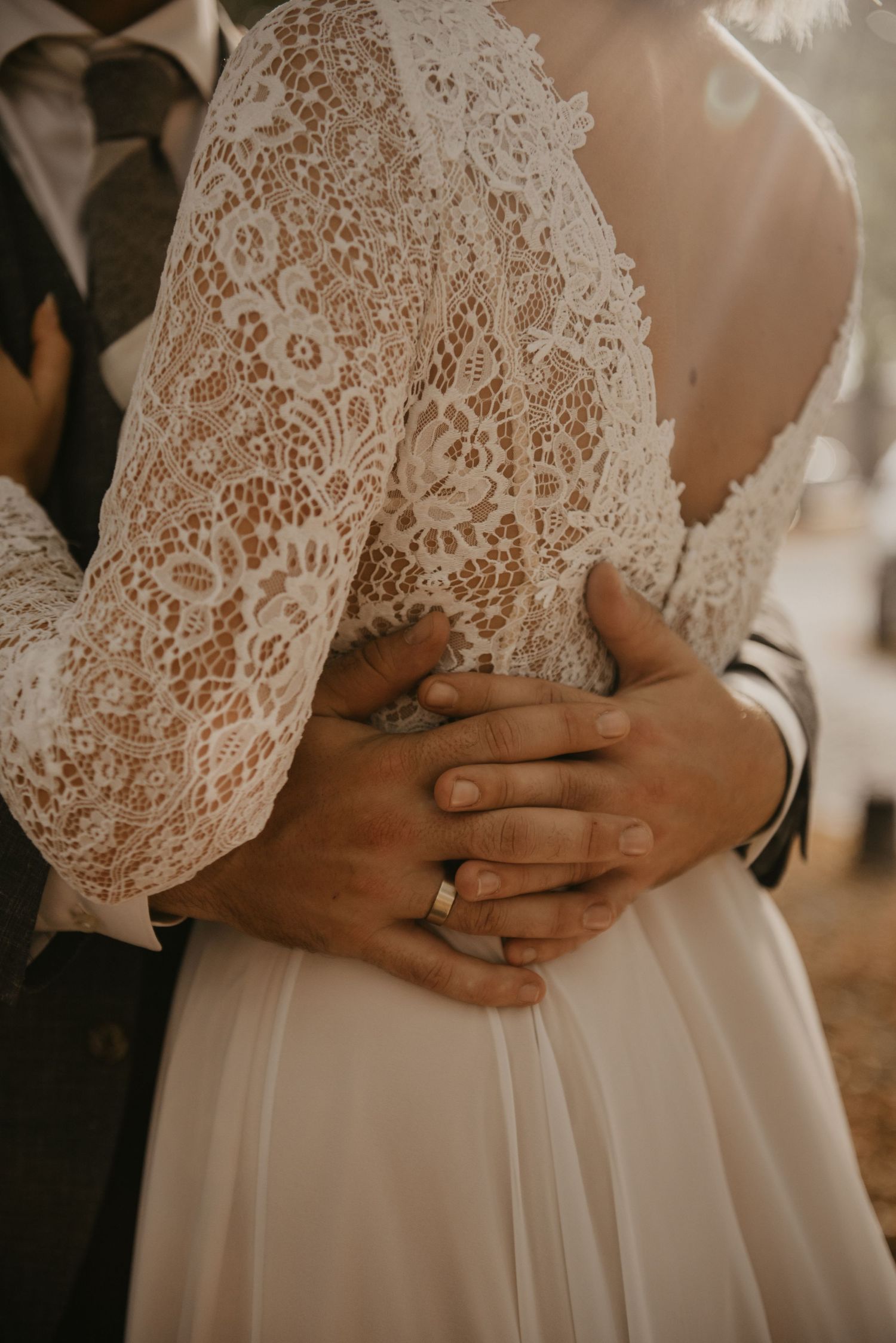Close-up of delicate lace wedding dress details with hands embracing.