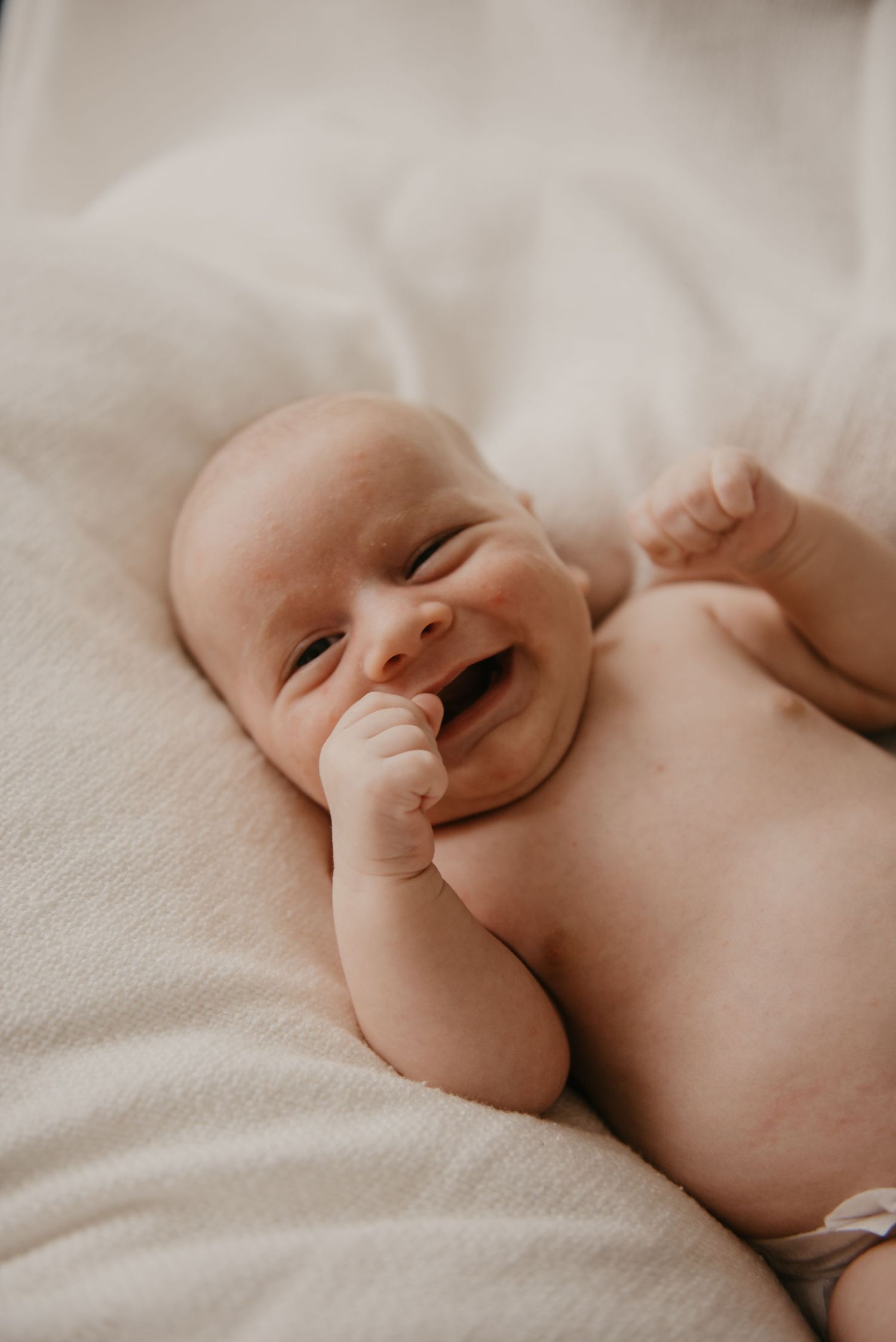 Joyful newborn baby lying on white textured blanket.