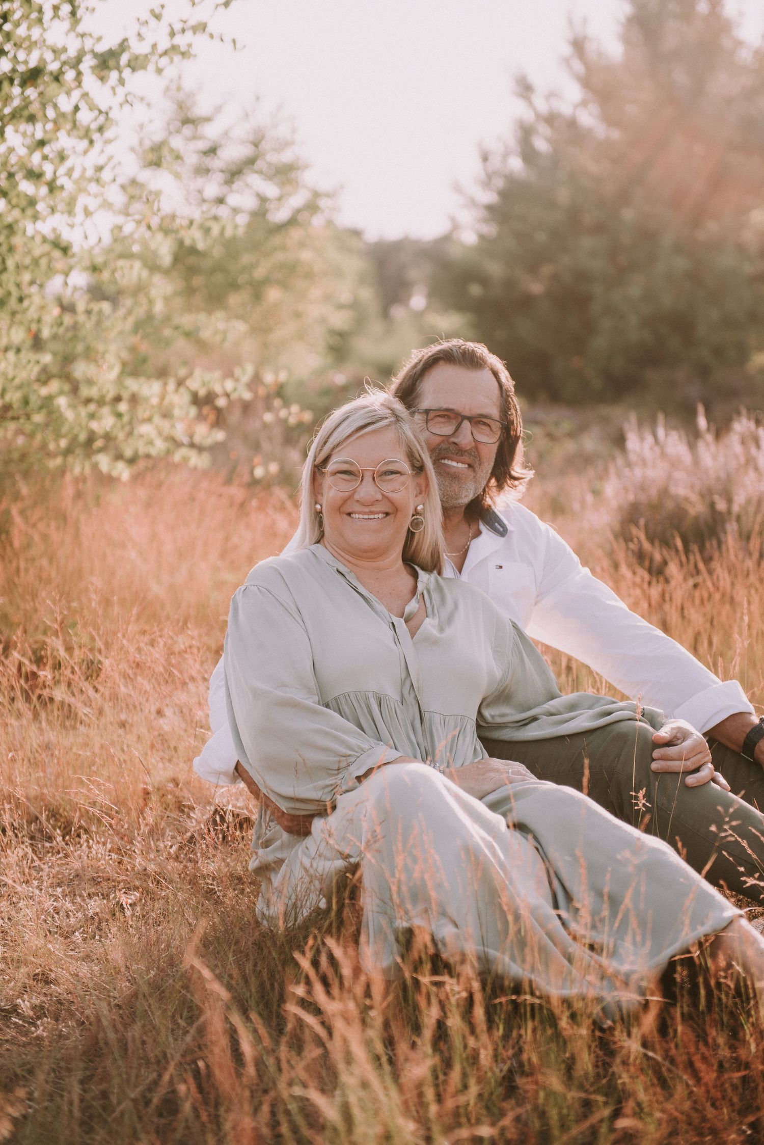 Couple relaxing together in tall grass during sunset photoshoot.