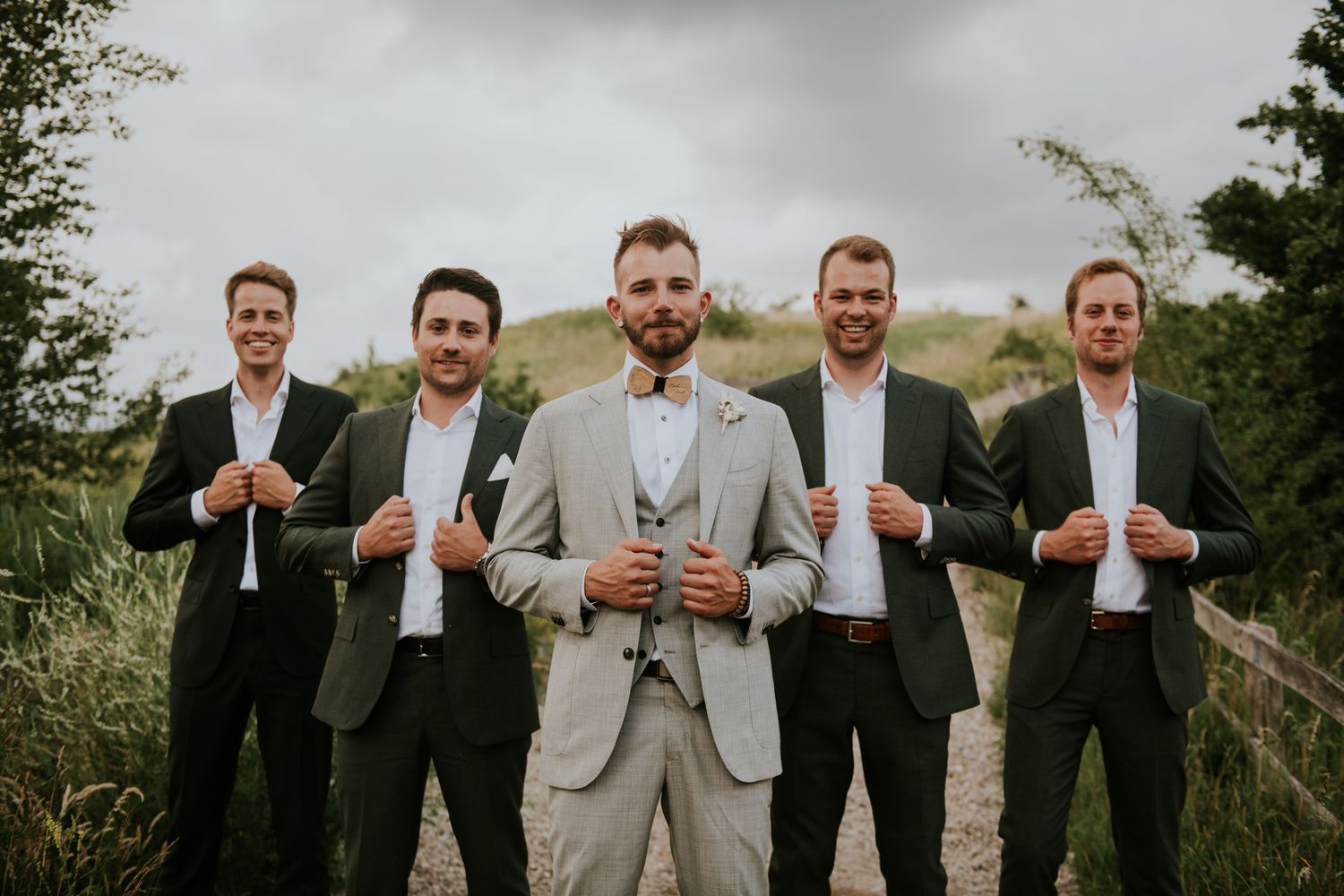 Groomsmen in gray suits pose together outdoors for wedding party photo.