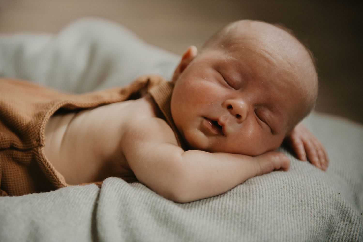 Peaceful sleeping newborn baby wearing brown clothing on soft gray blanket.