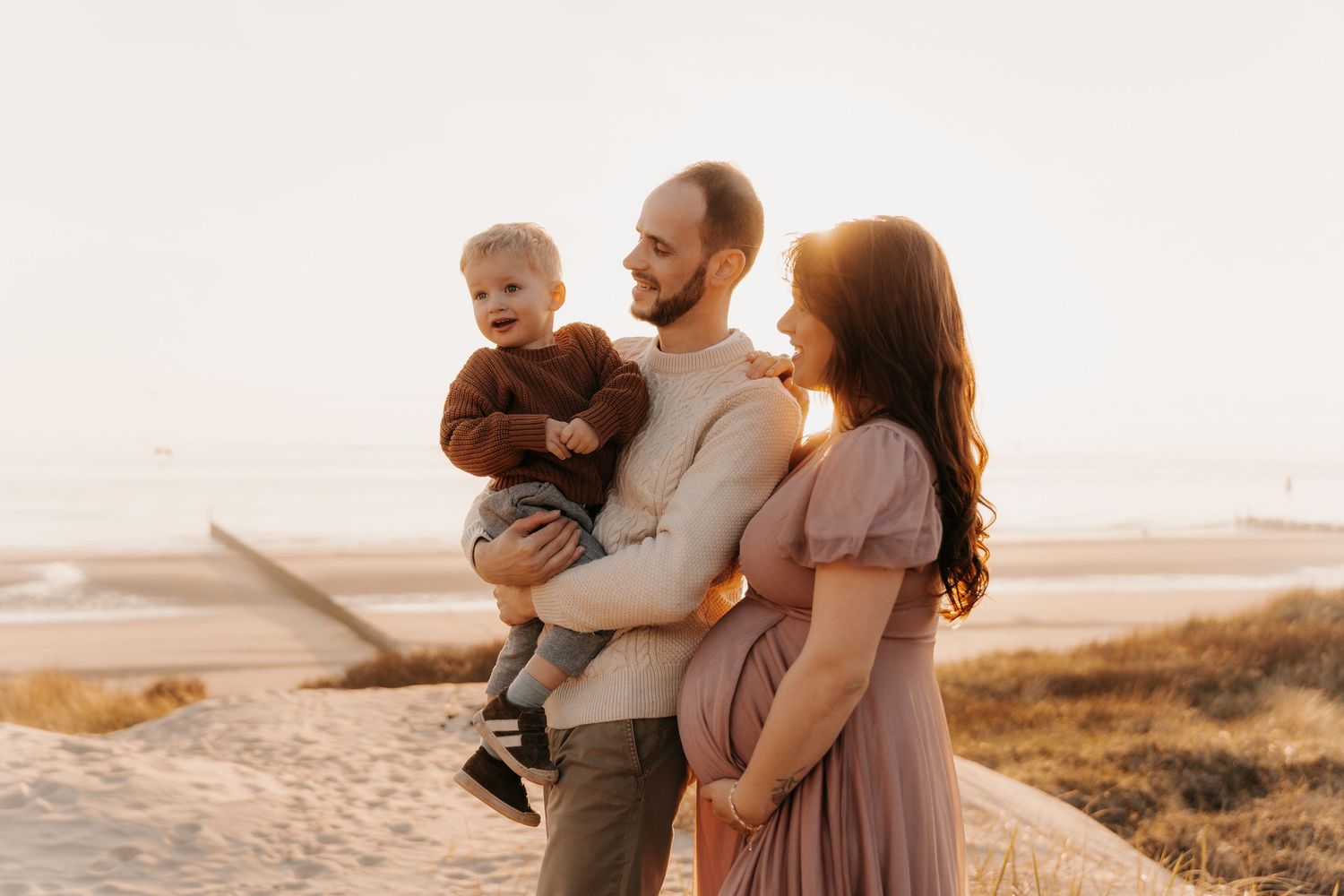 Family enjoying a sunset moment together on a beach with warm golden light.