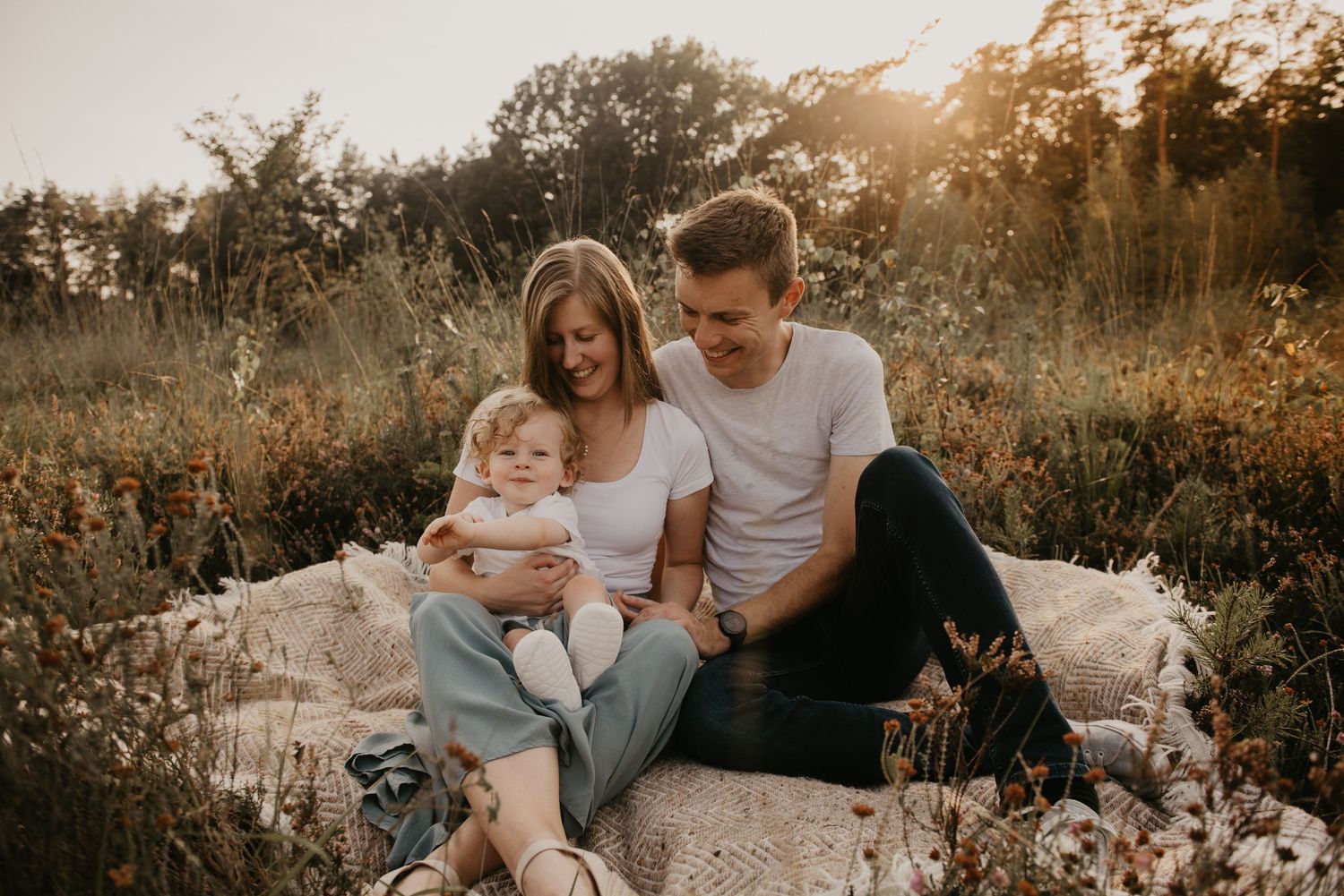 A family shares intimate moments together on a blanket in nature during sunset.