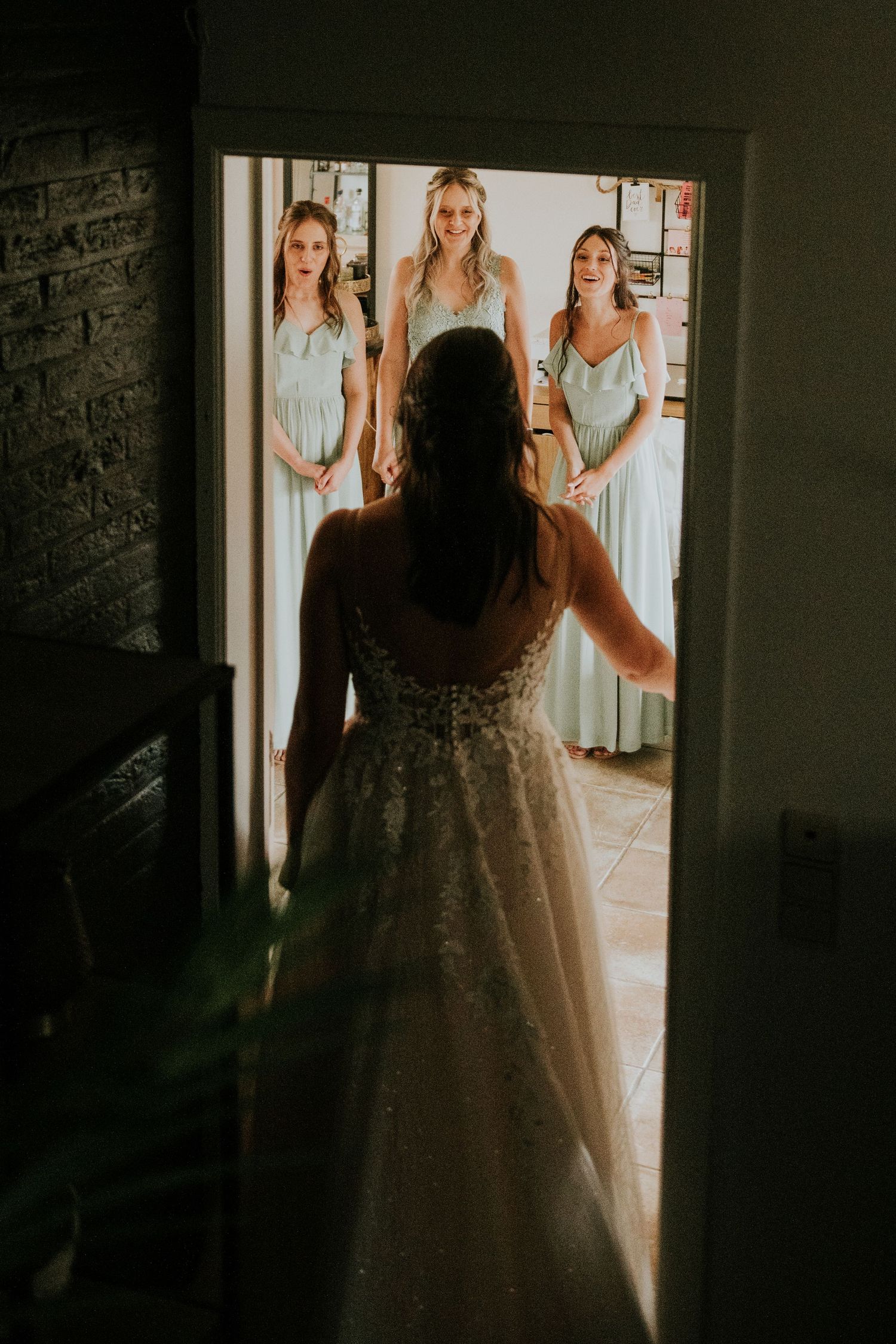 Getting ready scene showing wedding dress silhouette against bright doorway with bridesmaids.