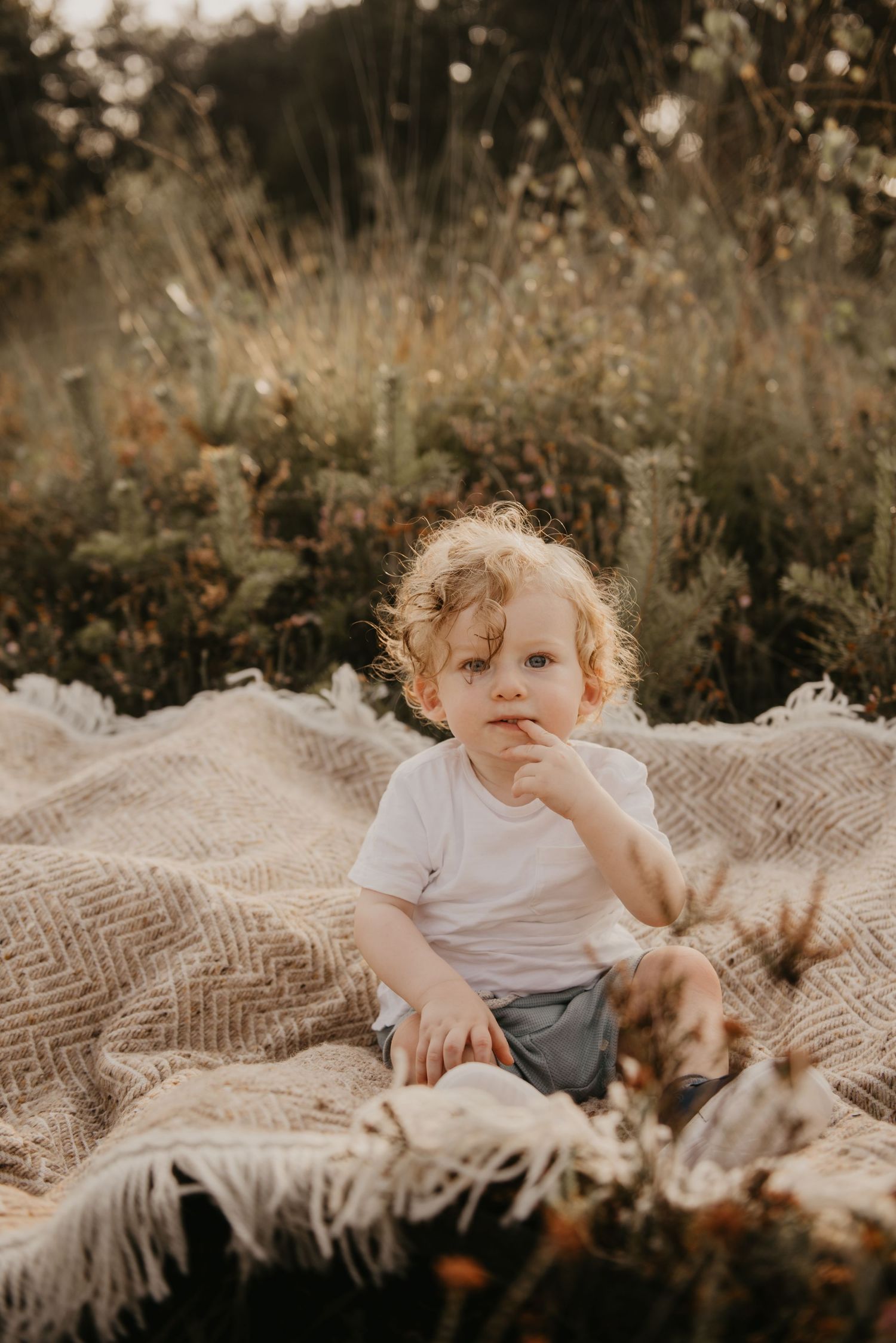 Child lying on a textured blanket outdoors surrounded by natural golden light.