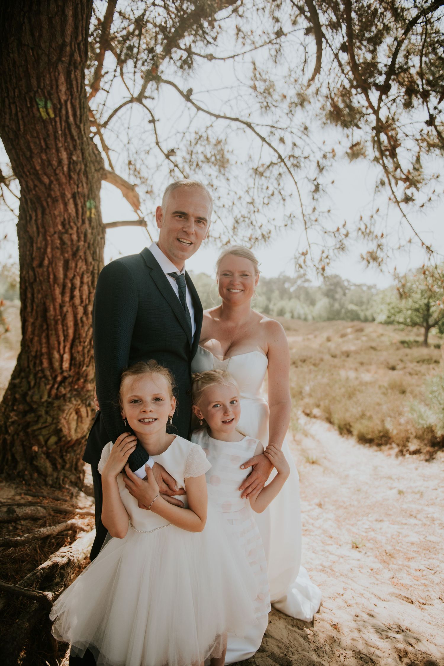 Wedding portrait under a large tree with flower girls in white dresses.
