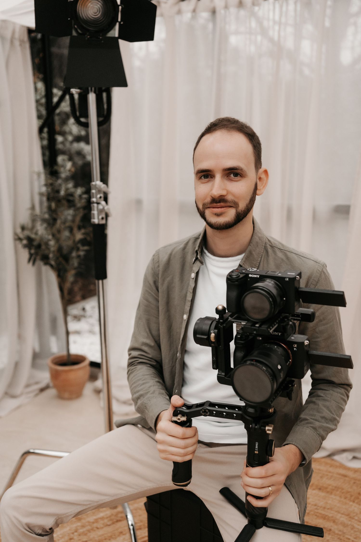 Videographer holding professional camera rig while posing in bright studio setting.