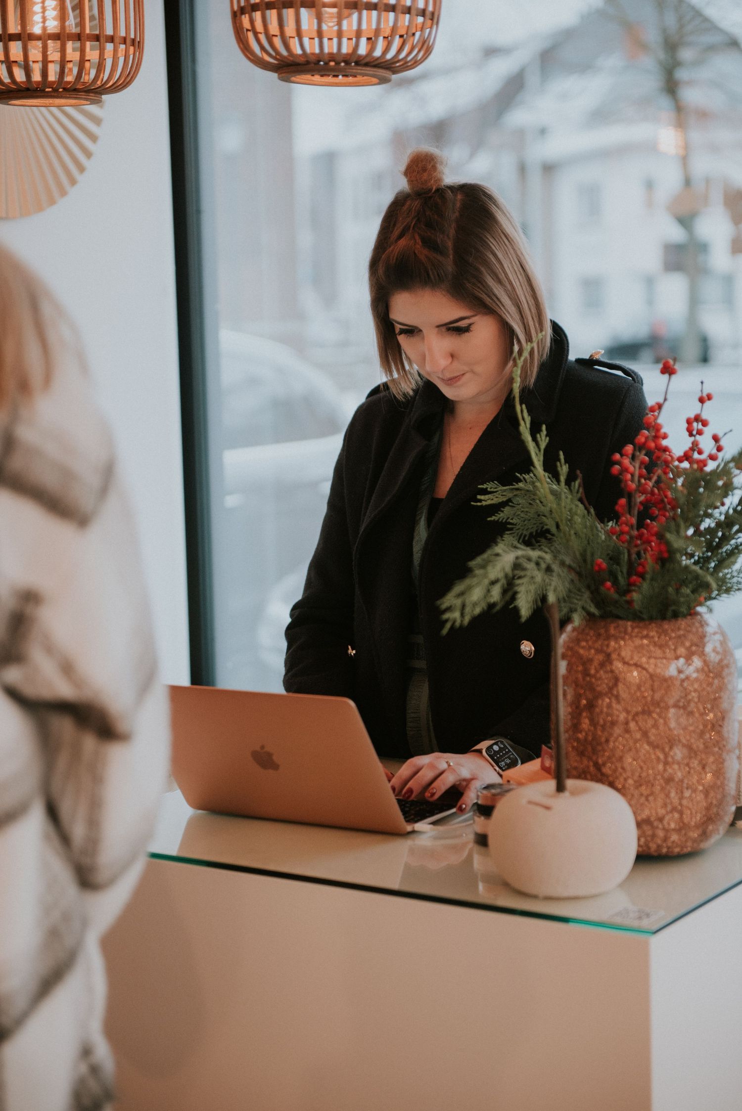 Person working on laptop at desk with festive holiday decorations and pendant lights.